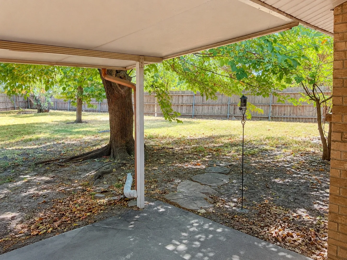 Covered patio with a concrete surface, mature trees, and a wood privacy fence