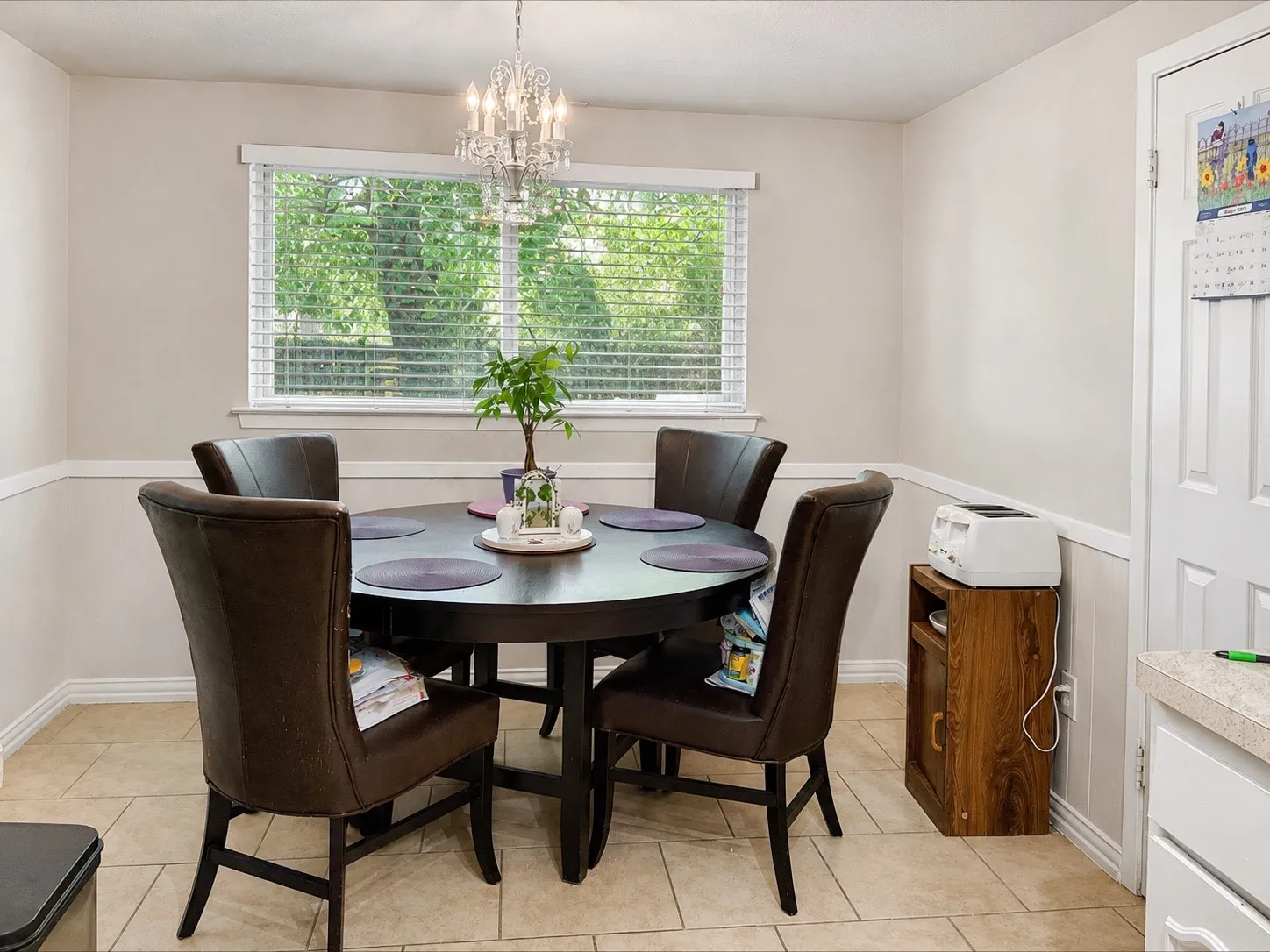 Recessed window with blinds, overhead chandelier, light-toned wall paint, decorative wainscoting, and tile flooring