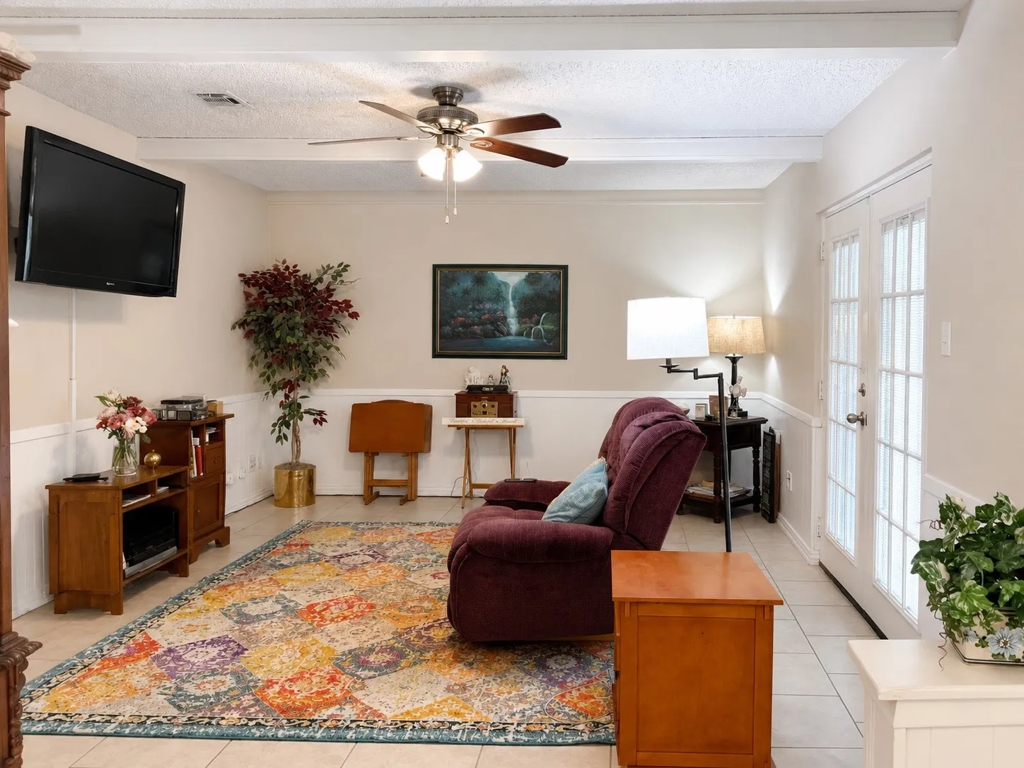 Ceiling fan with light fixture, white wood accent trim, white paneled double doors, tile flooring, and exposed white ceiling beams
