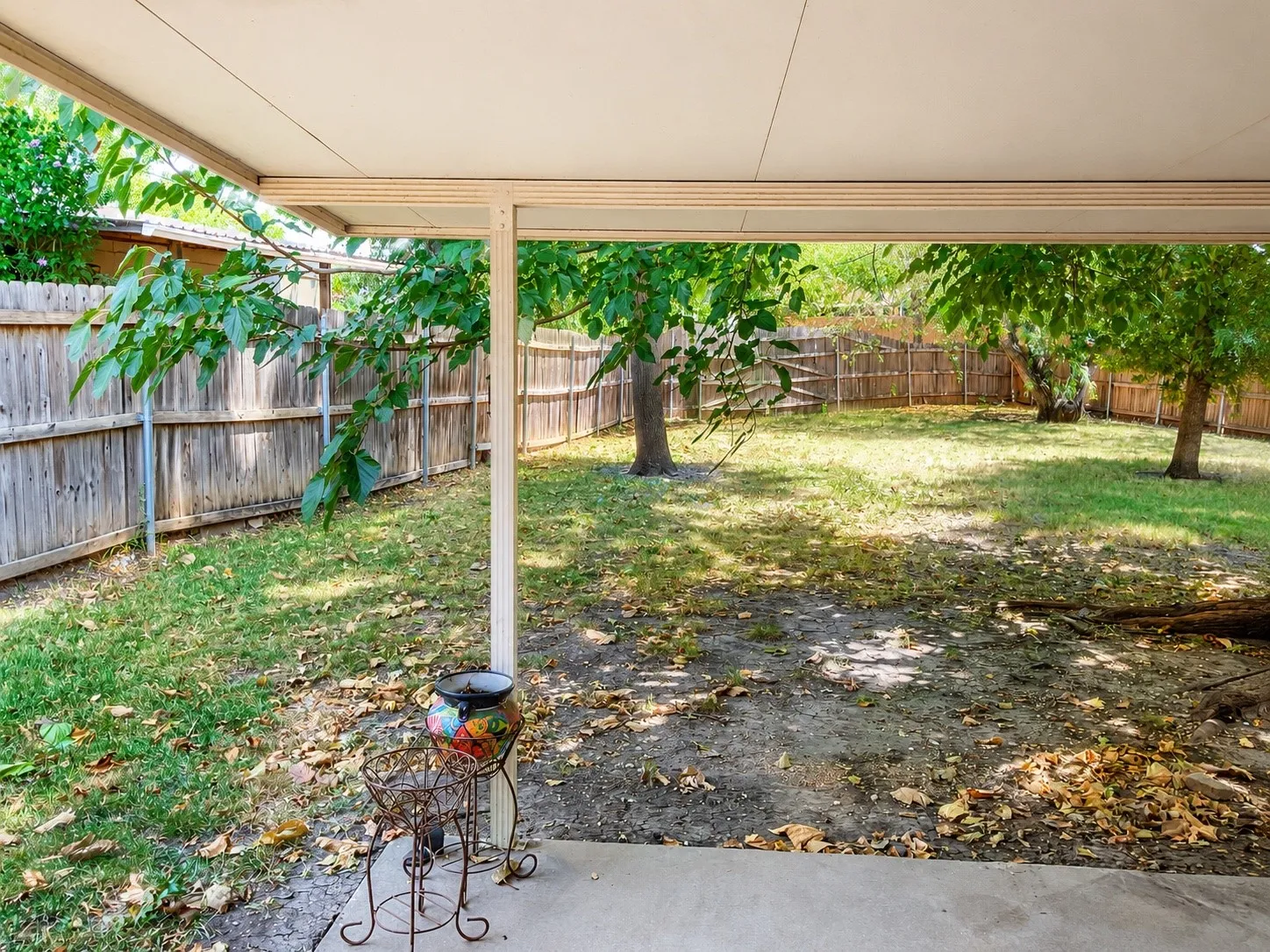 Covered patio with a concrete surface, expansive yard, and mature trees