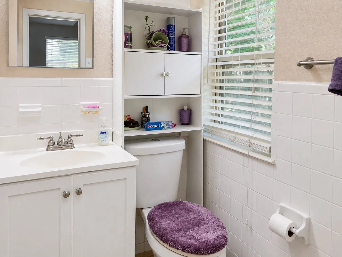 Built-in vanity with under-sink storage, mirrored medicine cabinet, white tiled walls, and over-toilet shelving