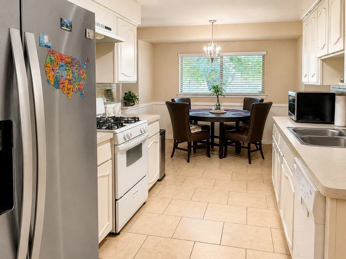 Kitchen featuring tile flooring, cream cabinetry, a stainless steel refrigerator, a white gas range, and a dual basin sink