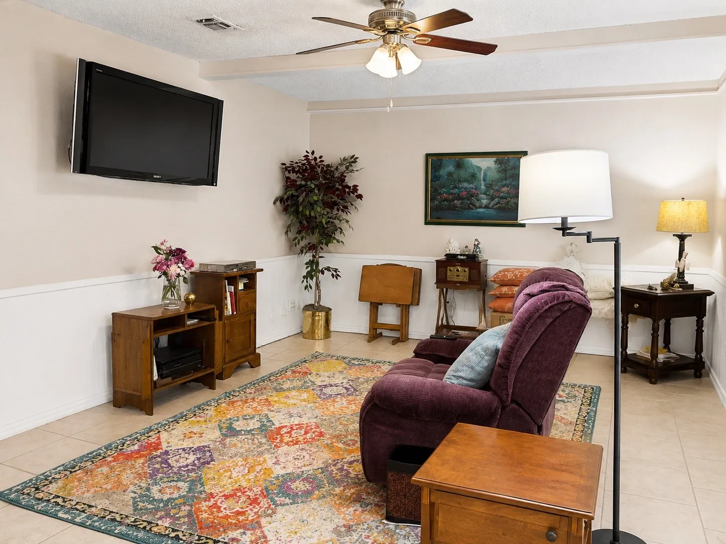 Recessed ceiling with a ceiling fan, light-toned tile flooring, and wainscoting