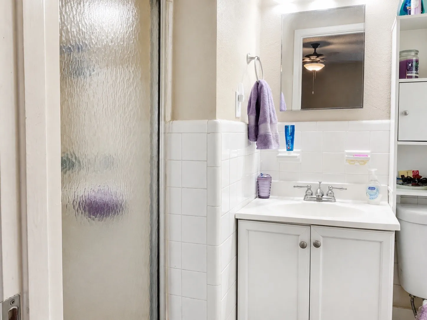 White tiled walls, built-in shelving, white vanity with integrated sink, and a framed mirror