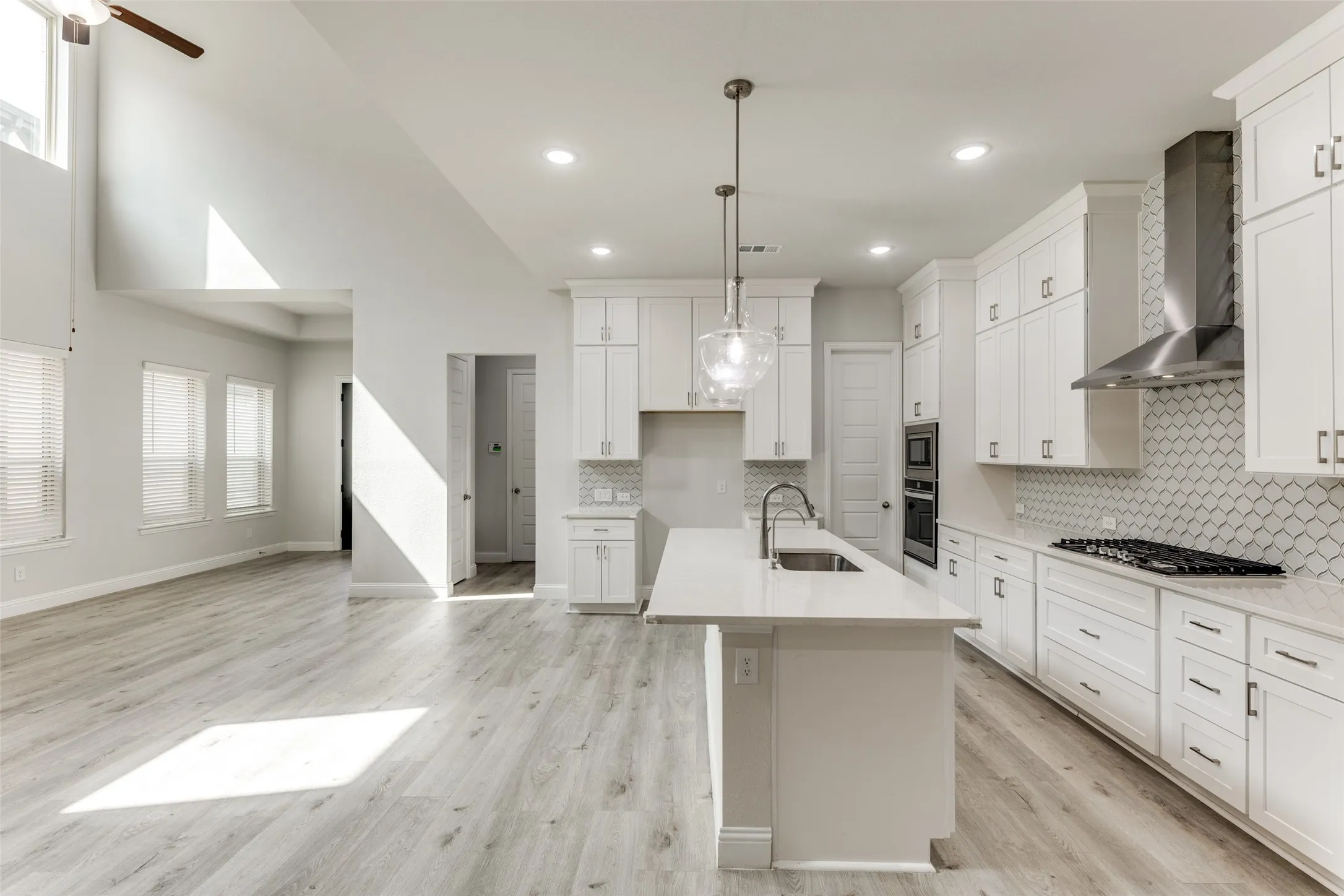 Kitchen with wall chimney range hood, a sink, stainless steel appliances, tasteful backsplash, and light countertops