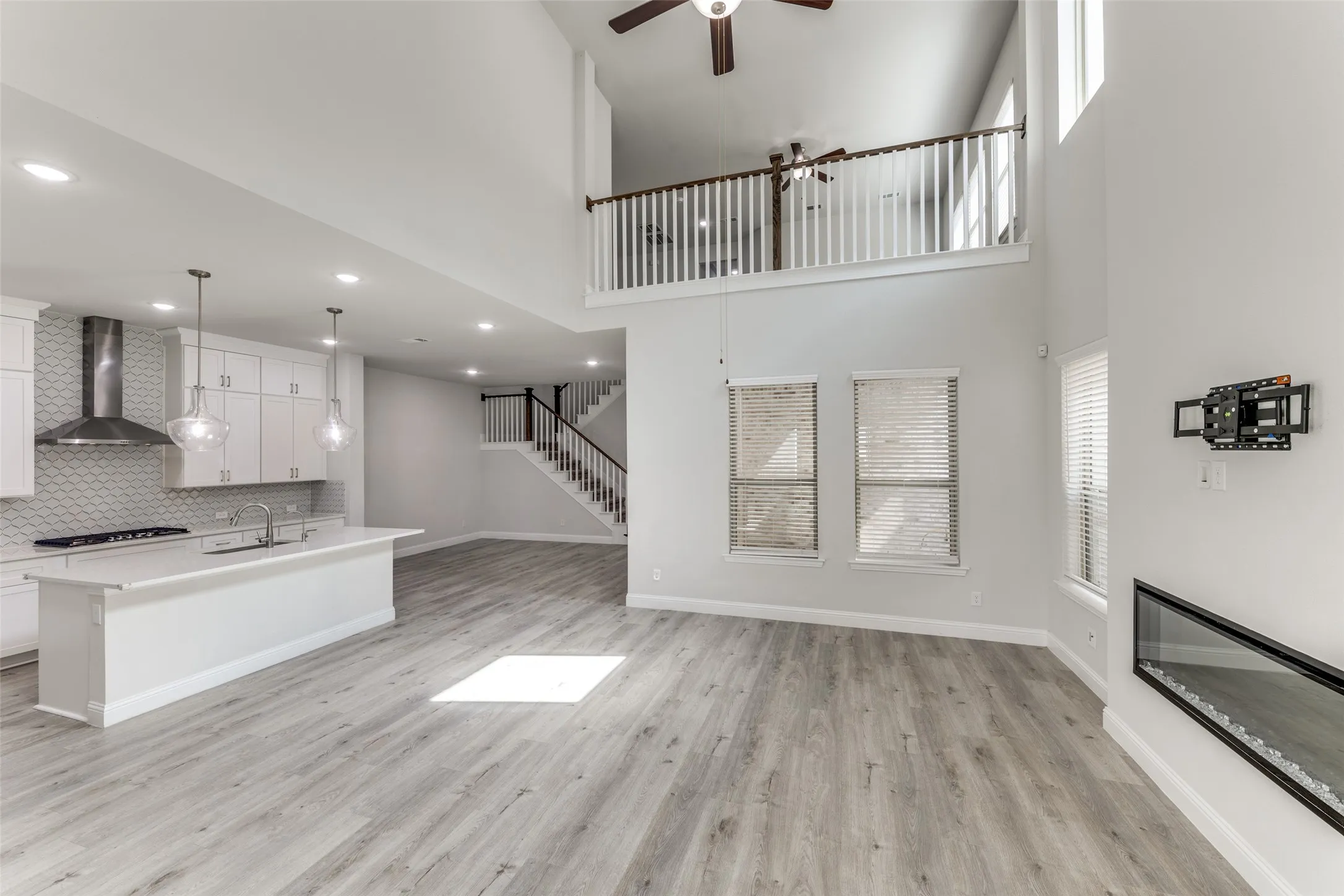 Unfurnished living room with a ceiling fan, light wood-style flooring, a high ceiling, a sink, and baseboards