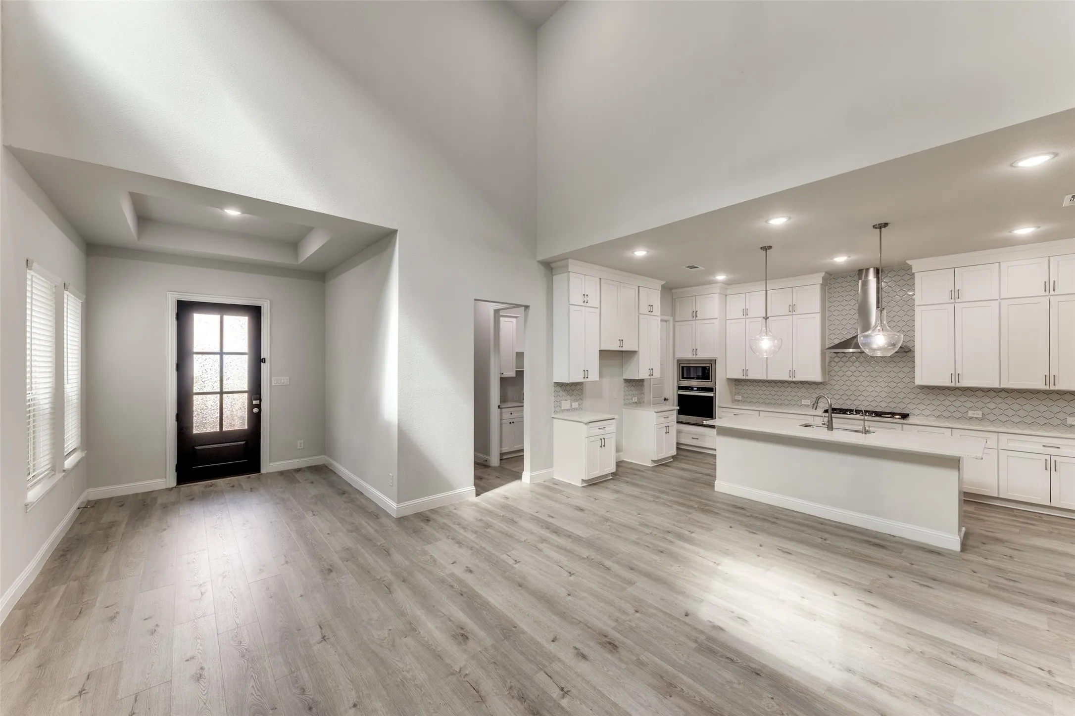Kitchen with wall chimney range hood, stainless steel appliances, light countertops, light wood-style flooring, and recessed lighting
