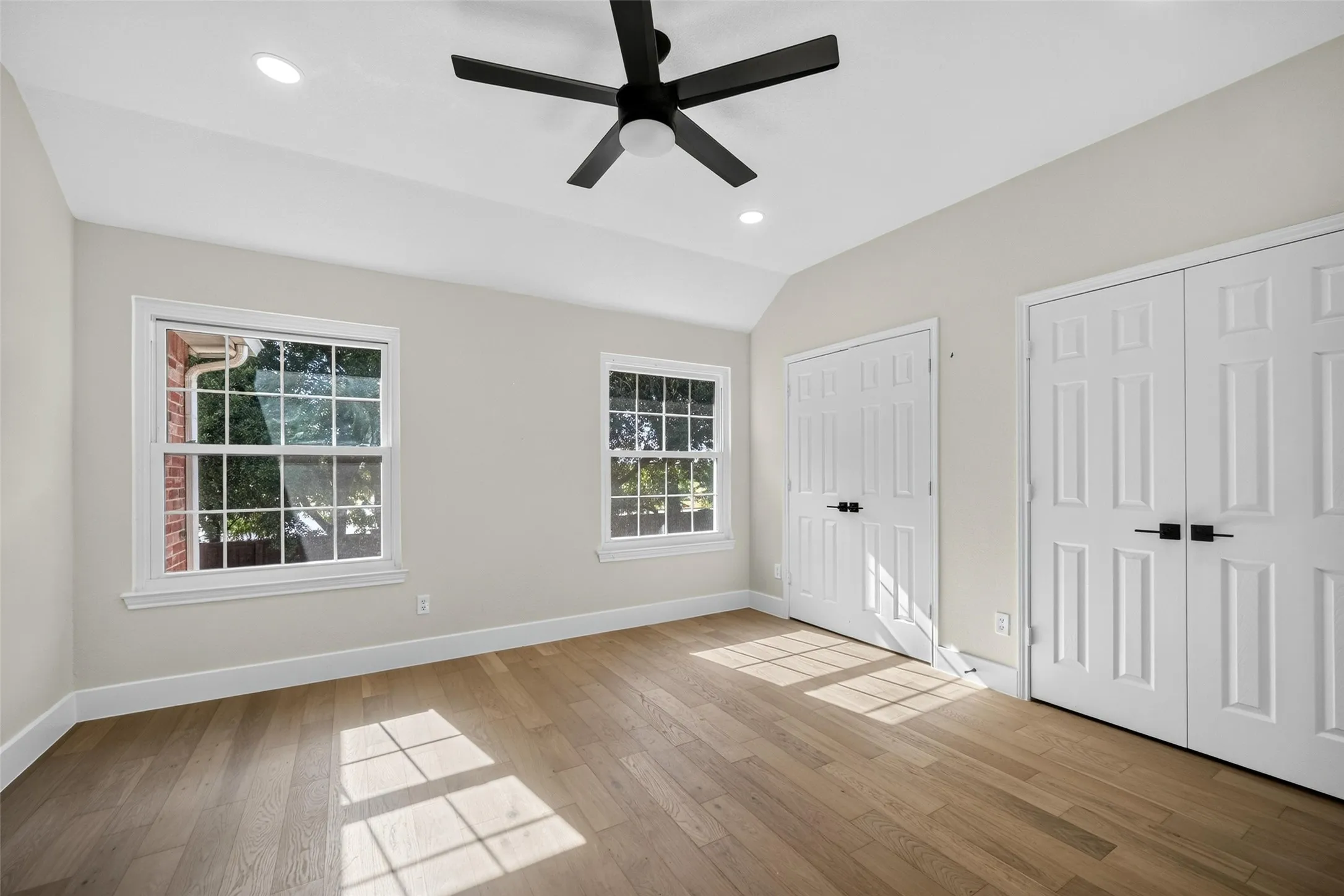 Vaulted ceiling with a ceiling fan, recessed lighting, wood-finish flooring, two double-door closets, and two windows