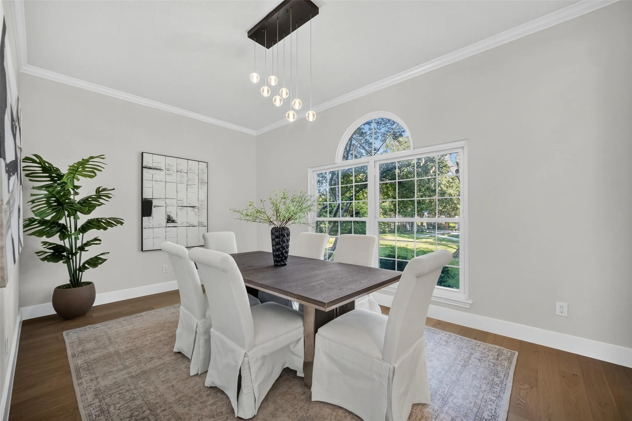Wood-finish flooring, crown molding, and a contemporary chandelier