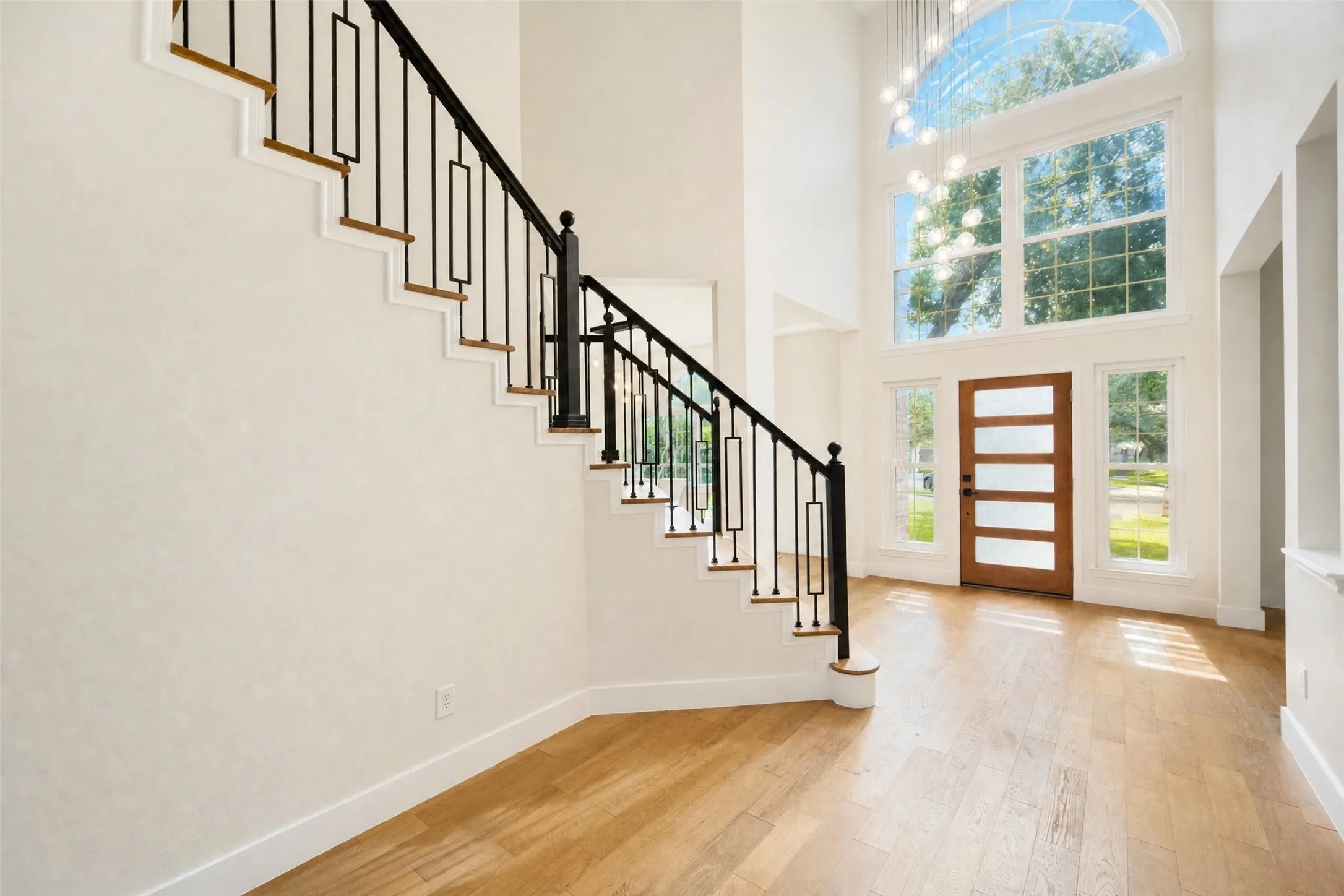 Two-story entryway featuring light wood-finish flooring, a contemporary wood-panel entry door, and a grand staircase with wrought iron balusters and wood treads