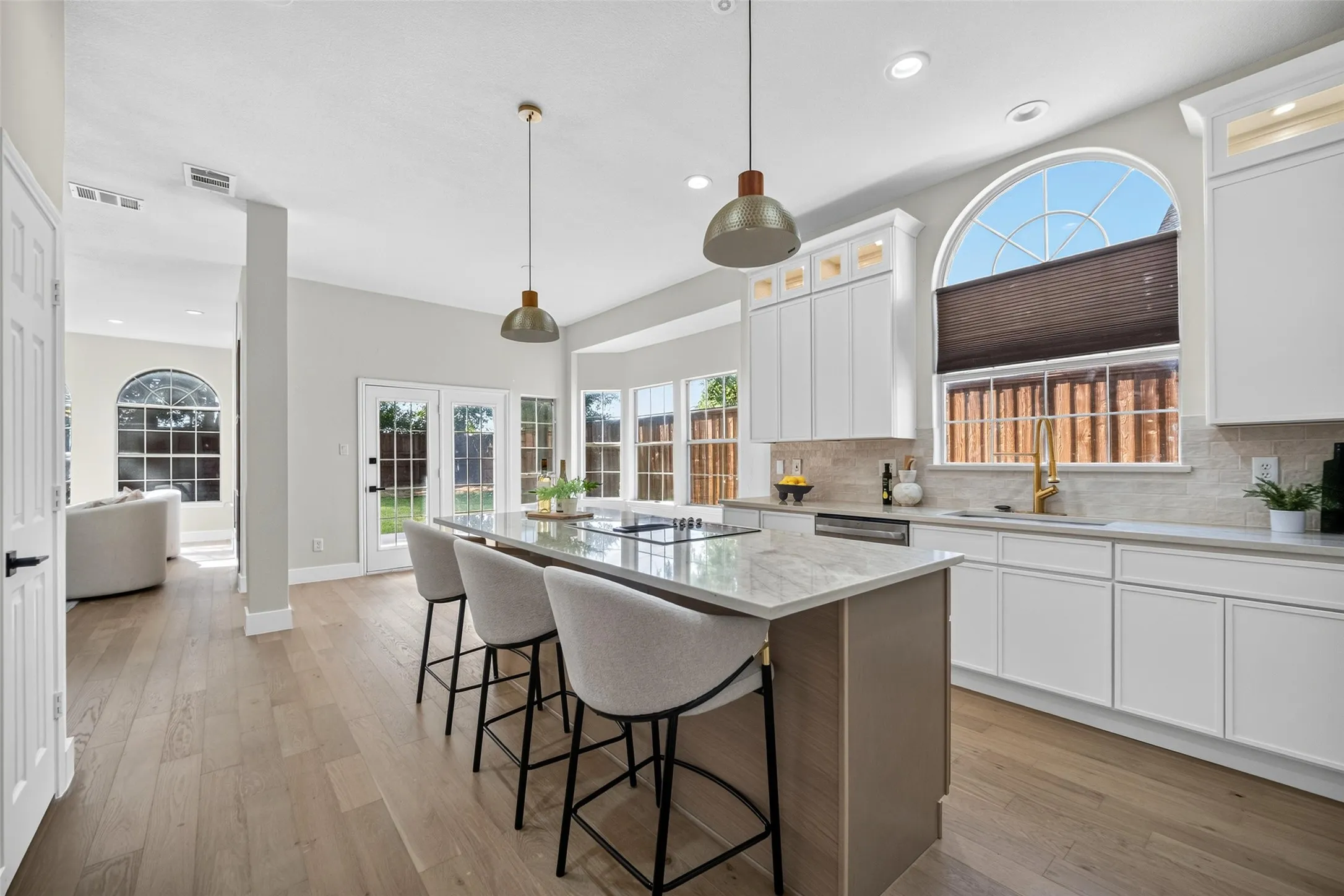 Kitchen with an island featuring a cooktop and stone countertop, white shaker-style cabinetry, wood-finish flooring, and French doors leading to the exterior