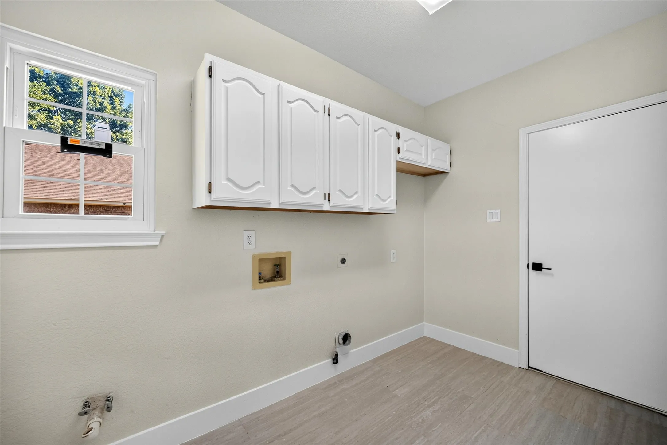 White cabinetry, wood-finish flooring, white door with black hardware, and a window with natural​​‌​​​​‌​​‌‌​‌‌​​​‌‌​‌​‌​‌​​​‌​​ light