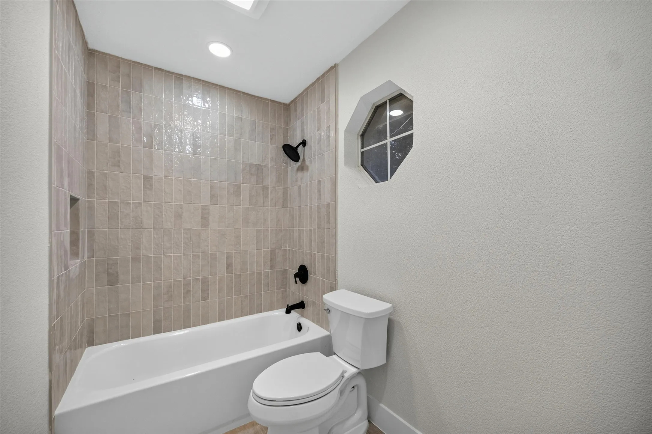 Bathtub with tiled surround, recessed shower niche, and matte black fixtures