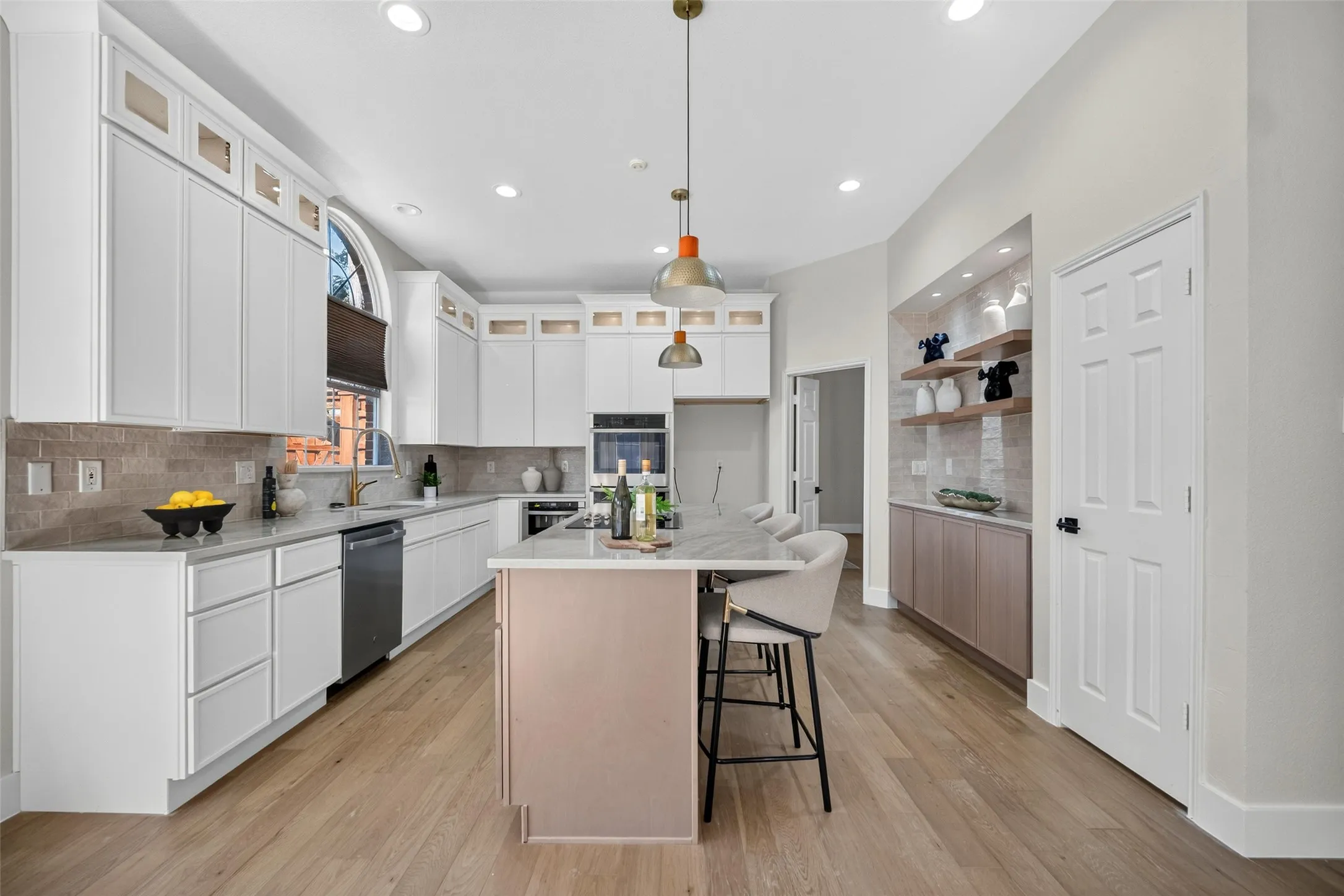 Spacious kitchen featuring white cabinetry, light wood-finish flooring, a center island with seating, a built-in oven, and recessed lighting