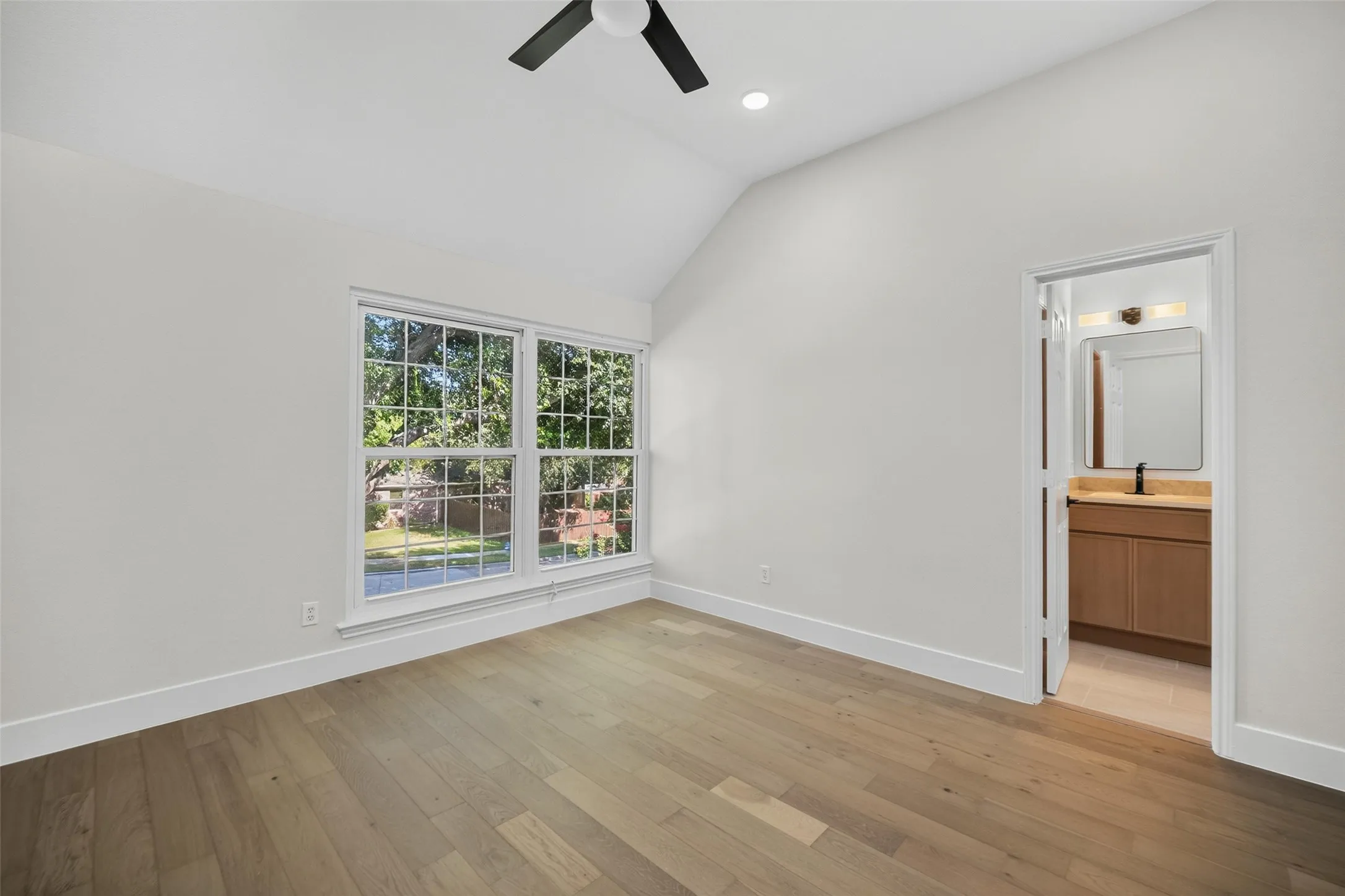 Vaulted ceiling with a ceiling fan, wood-finish flooring, and a double window