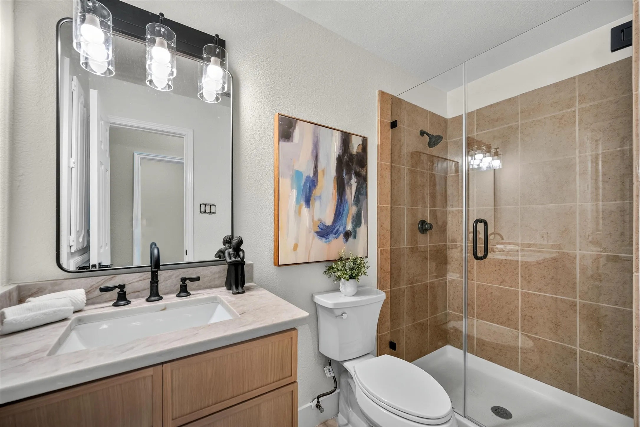 Bathroom featuring a glass-enclosed shower, light wood-finish vanity with an undermount sink, stone-finish countertop, and black-finish fixtures