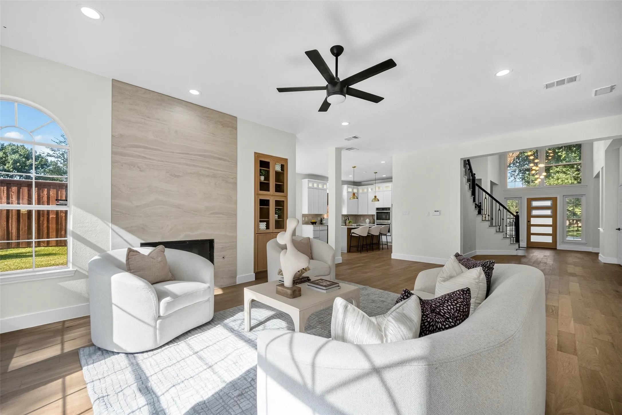 Spacious living area featuring a wood-finish flooring, a contemporary fireplace with a stone surround, recessed lighting, and a modern ceiling fan