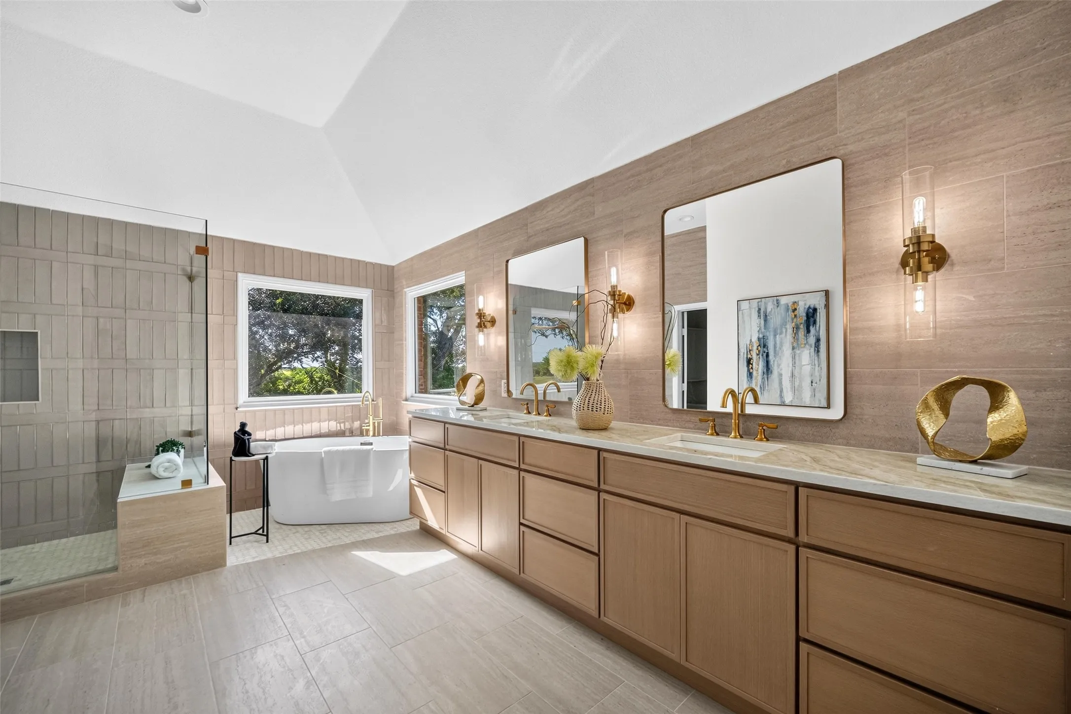 Vaulted ceiling with recessed lighting, double vanity with wood-finish cabinetry, frameless mirrors with wall sconces, freestanding soaking tub, and a glass-enclosed shower with bench seating