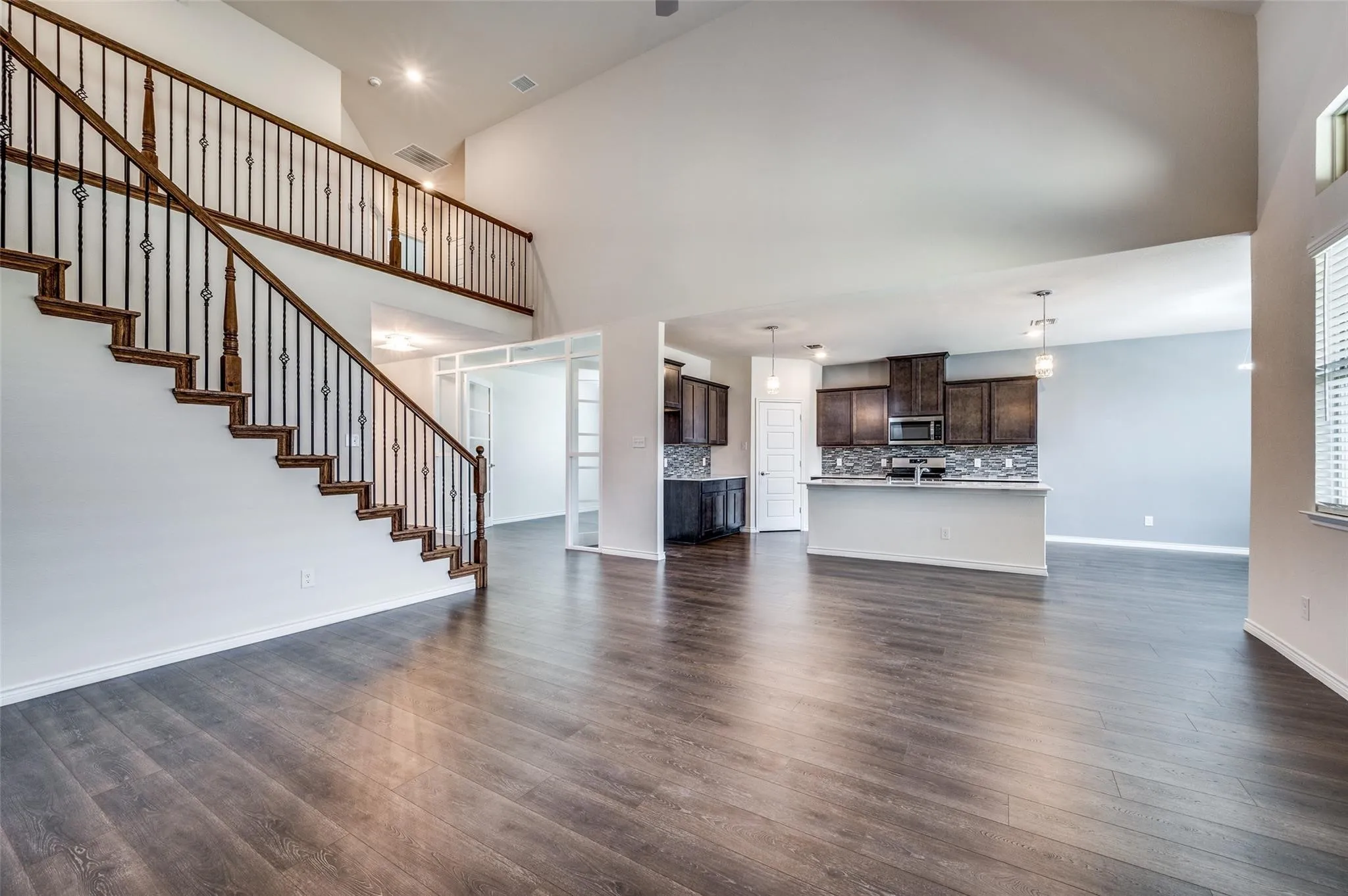 High-ceiling interior with wood-finish flooring, a kitchen island, dark wood cabinetry, and a wrought iron staircase