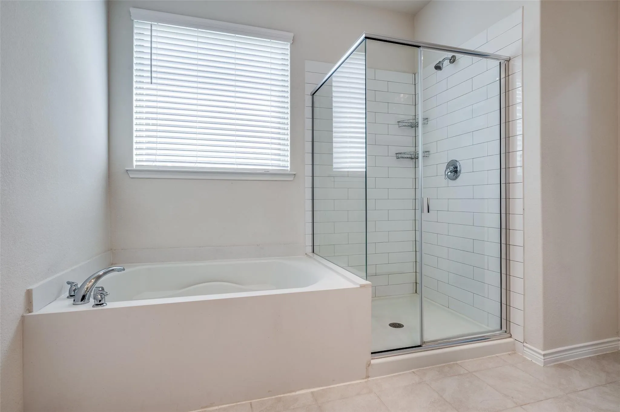 Built-in bathtub with chrome fixtures, glass-enclosed shower with subway tile surround, and light-toned floor tile