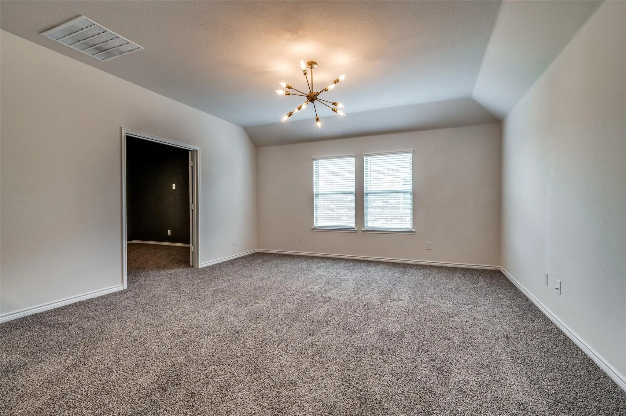 Vaulted ceiling with a contemporary light fixture, dual windows with blinds, and neutral carpeting