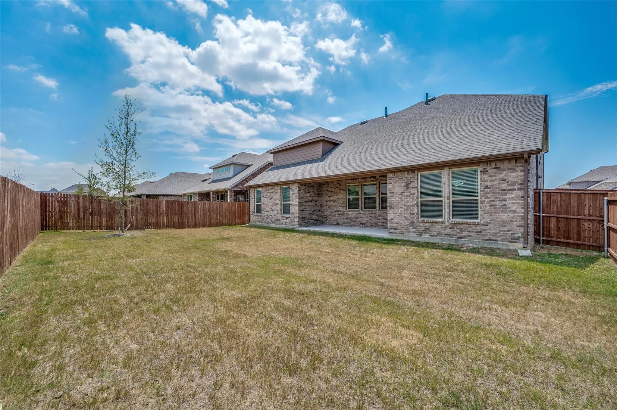 Spacious backyard featuring a full privacy fence, brick exterior, covered patio, and multi-pane windows