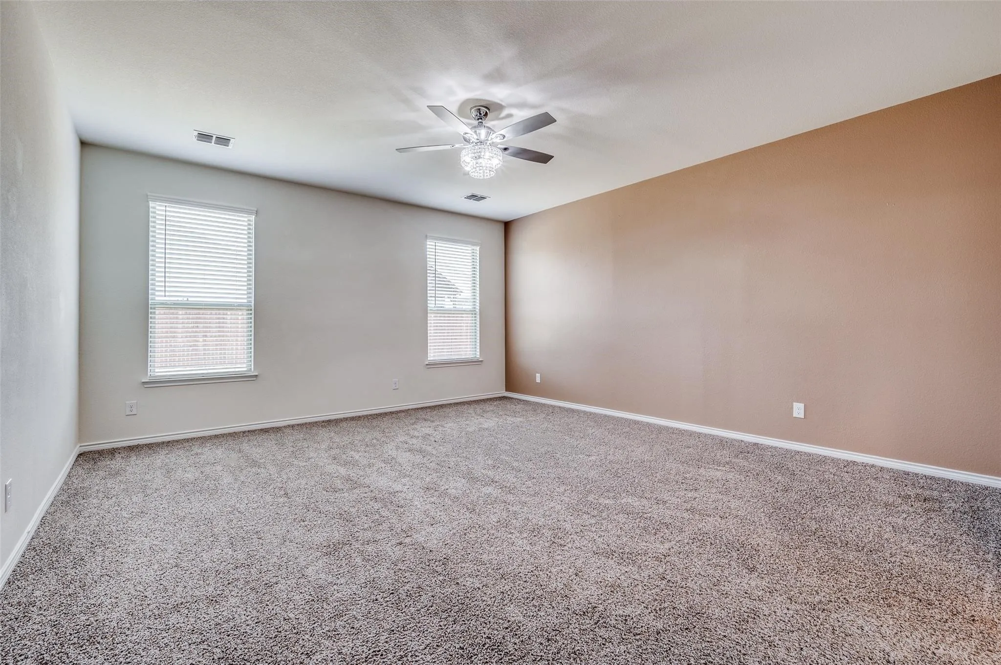 Spacious room featuring neutral carpeting, a ceiling fan with integrated lighting, and two windows with blinds