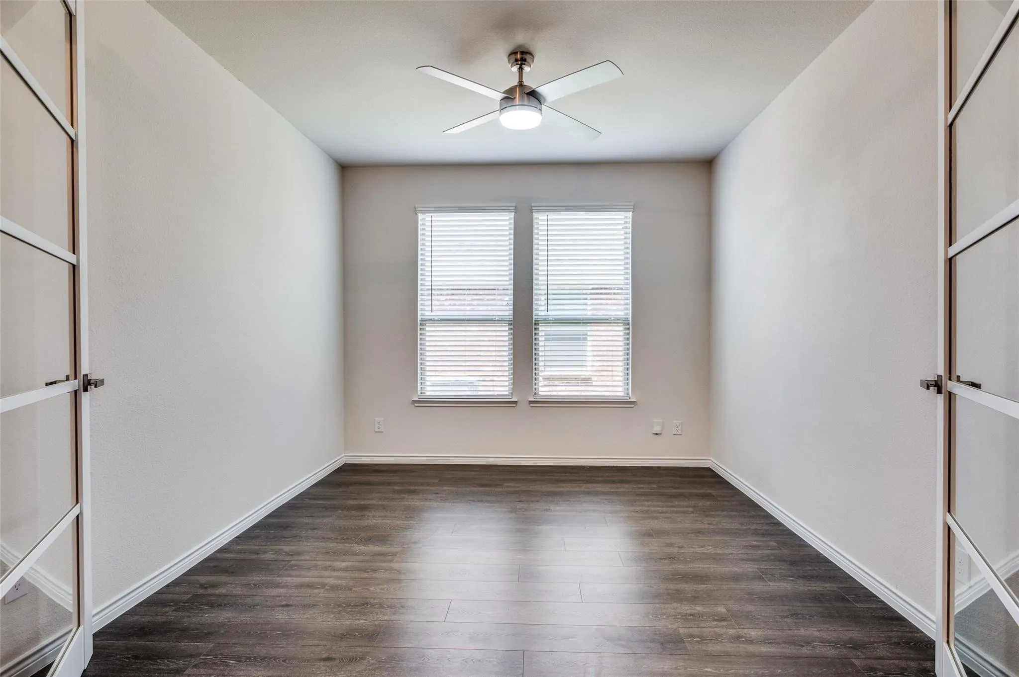 Wood-finish flooring, dual windows with blinds, and a ceiling fan with integrated lighting