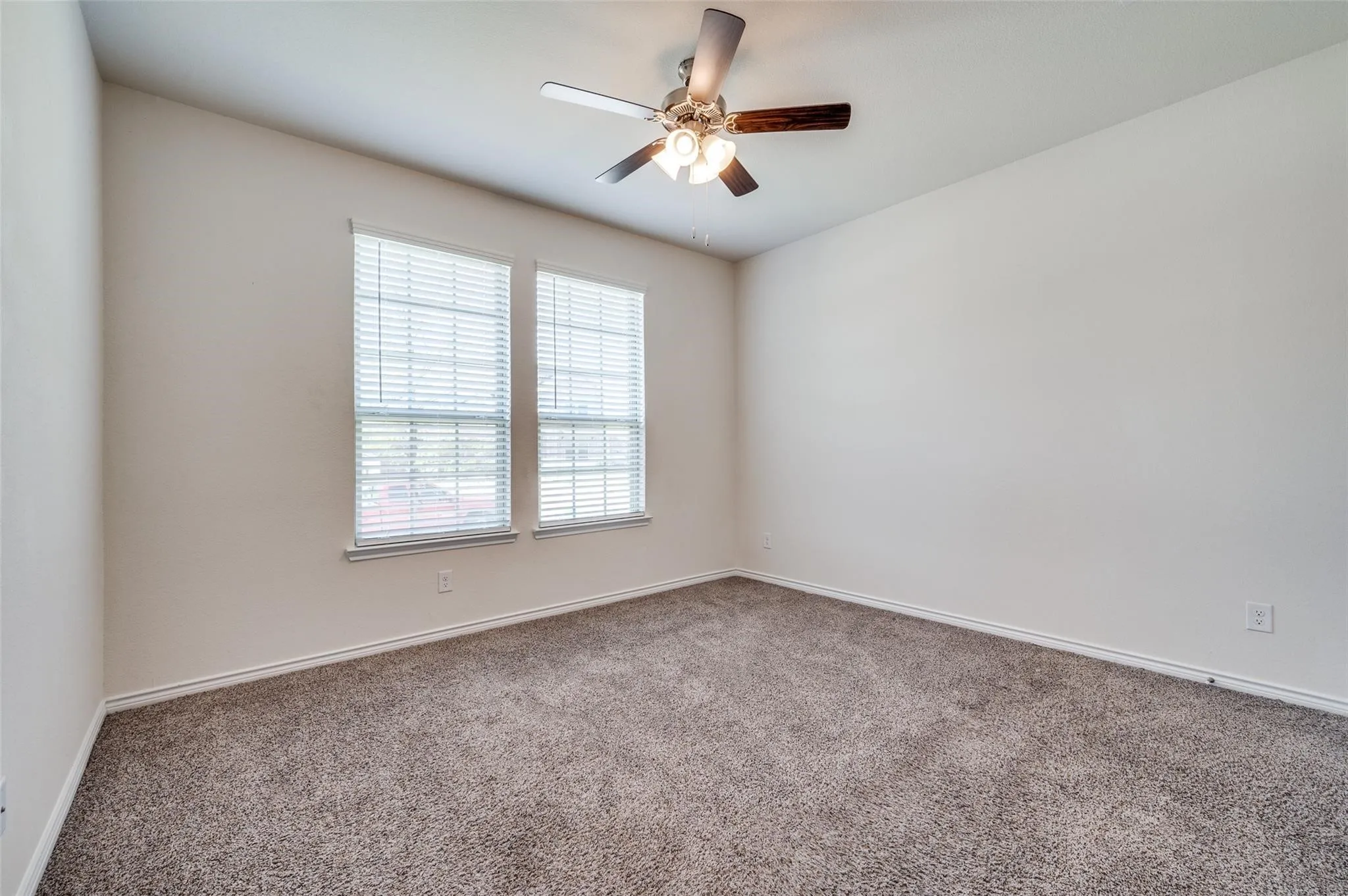 Neutral wall finishes, textured carpet flooring, two windows with blinds, and a ceiling fan with integrated lighting