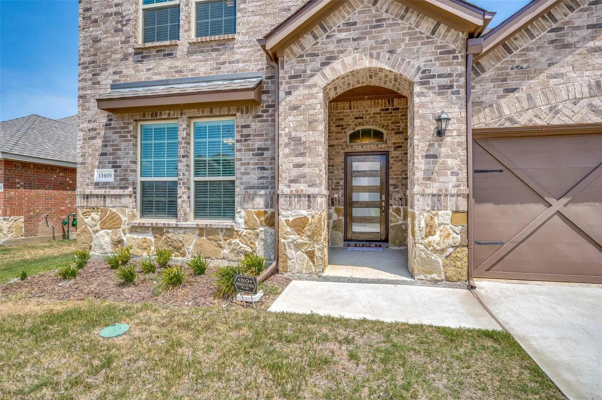 Brick and stone exterior with an arched entryway, modern glass-paneled entry door, and a carriage-style garage door