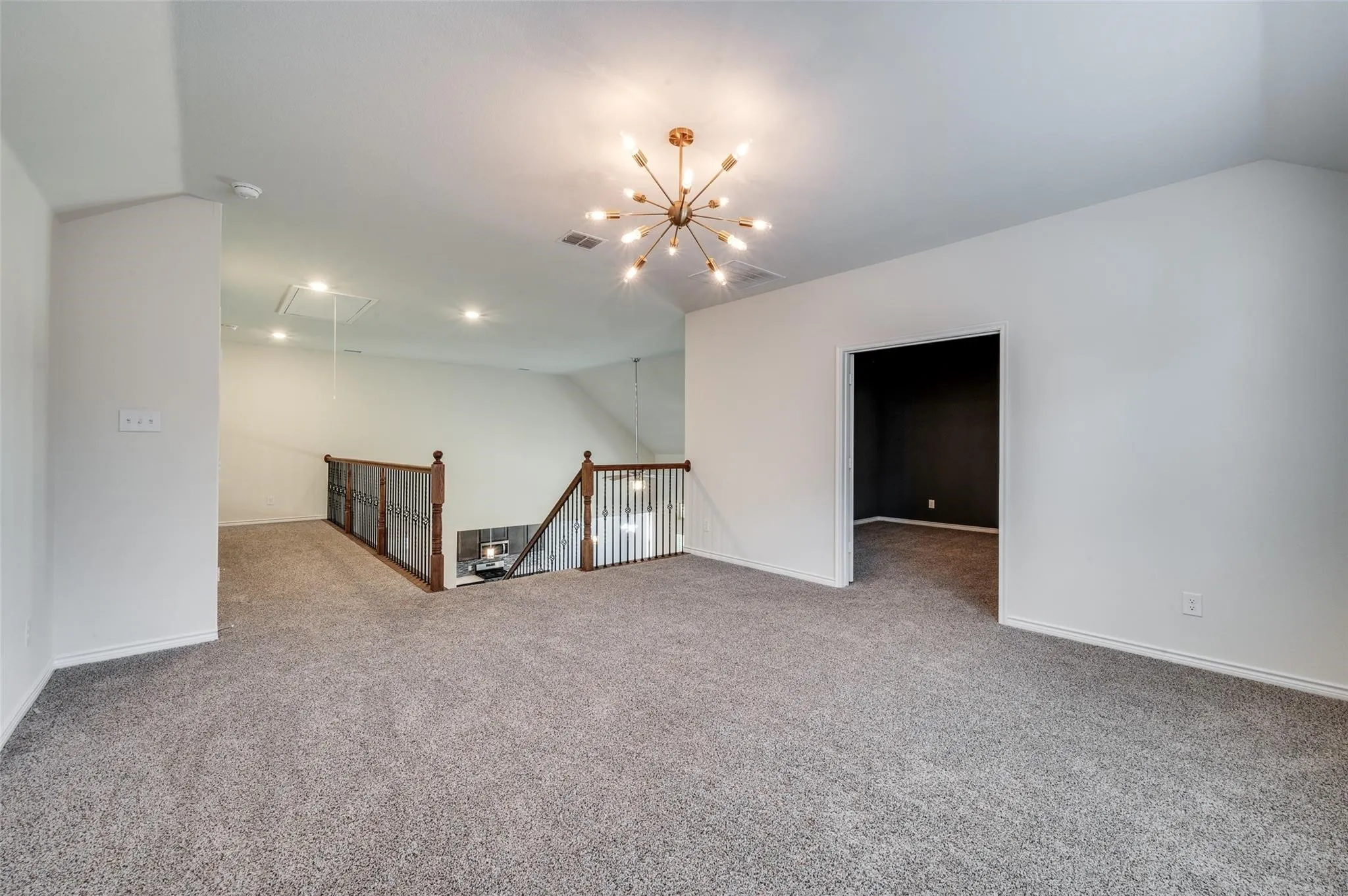 Carpeted loft area featuring a sputnik style chandelier, recessed lighting, and wood and wrought iron staircase railing