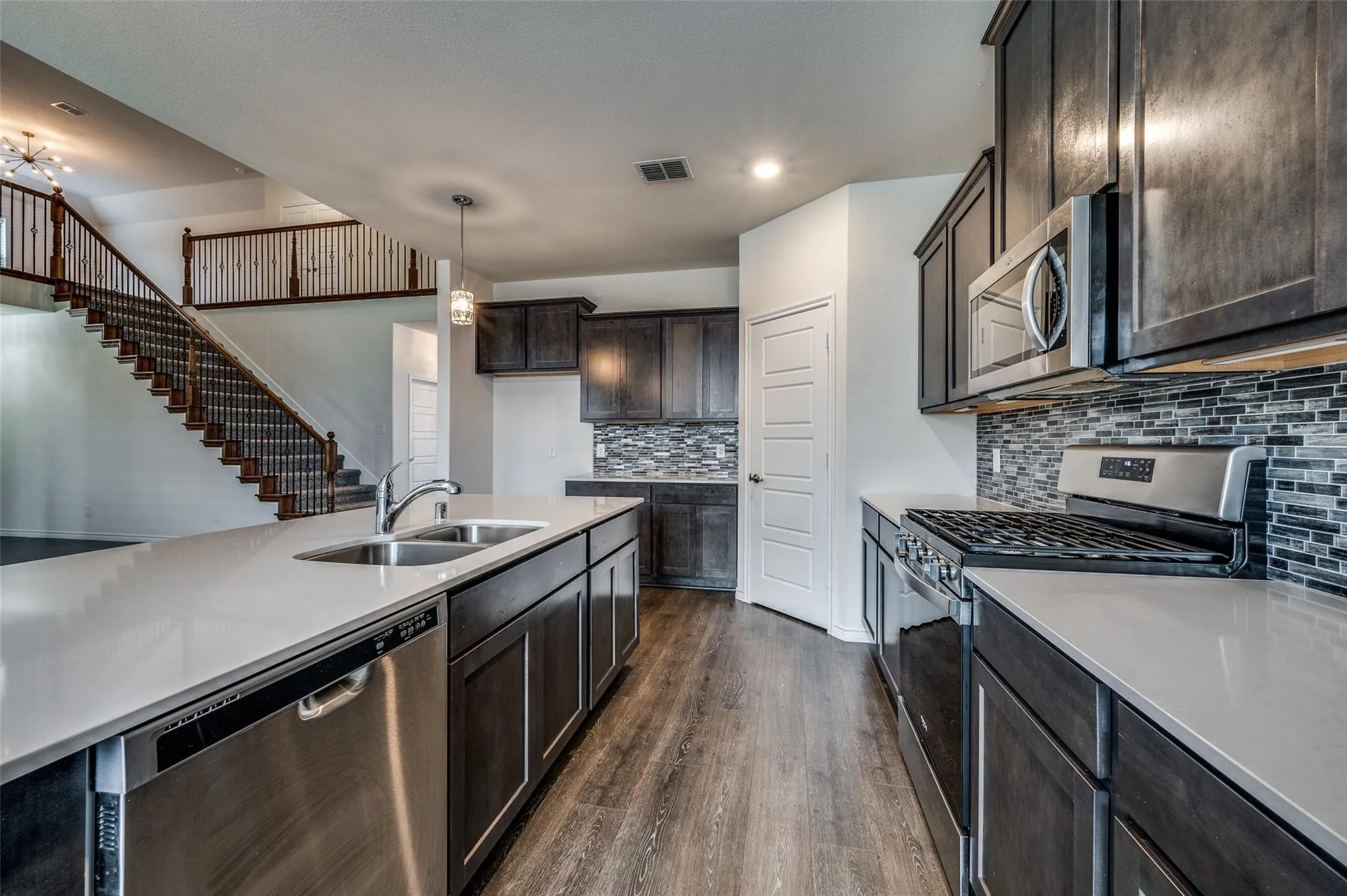 Kitchen featuring an island with dual basin sink, stainless steel appliances, dark wood-finish cabinetry, and mosaic tile backsplash