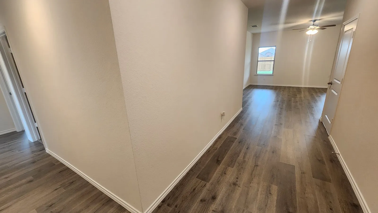 Wood-finish flooring throughout, light-colored walls, ceiling fan with integrated lighting, and a window with backyard exposure
