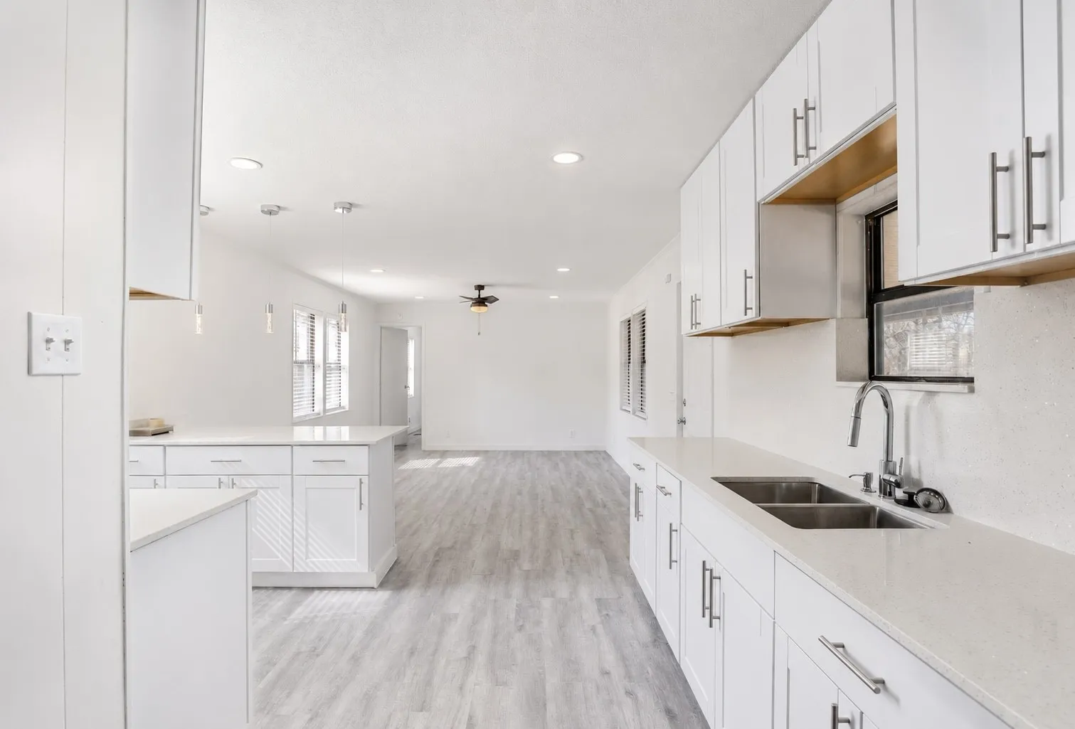 Kitchen featuring white shaker cabinetry, light-toned countertops, stainless steel double-basin sink with a gooseneck faucet, and recessed lighting