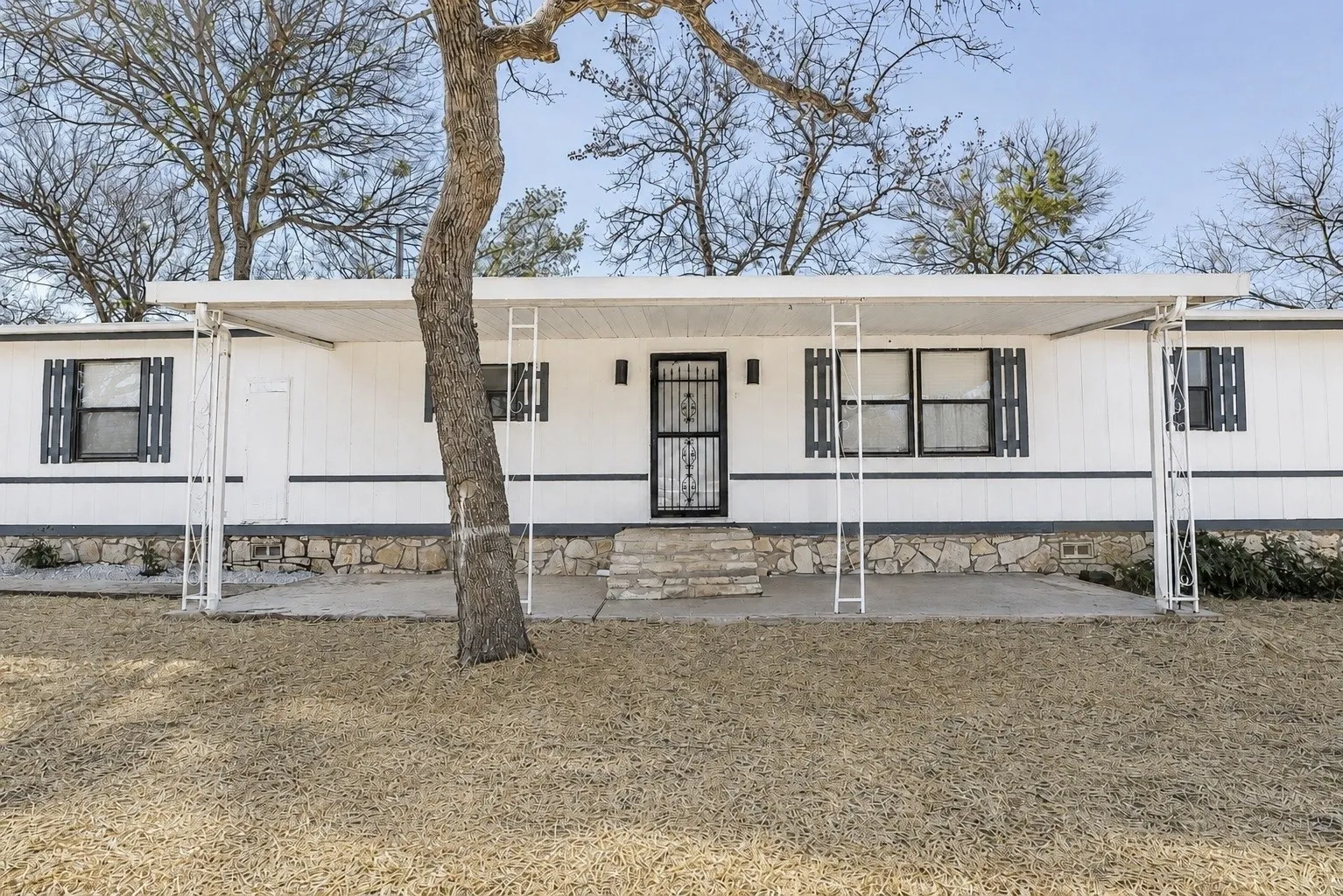 White siding exterior with a dark grey stone foundation, covered front porch with white metal supports, and dark shutters
