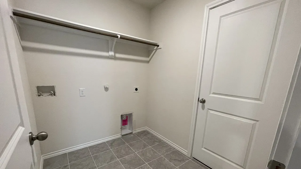 Utility area featuring a tile floor, white shaker-style door, and built-in shelving with a hanging rod