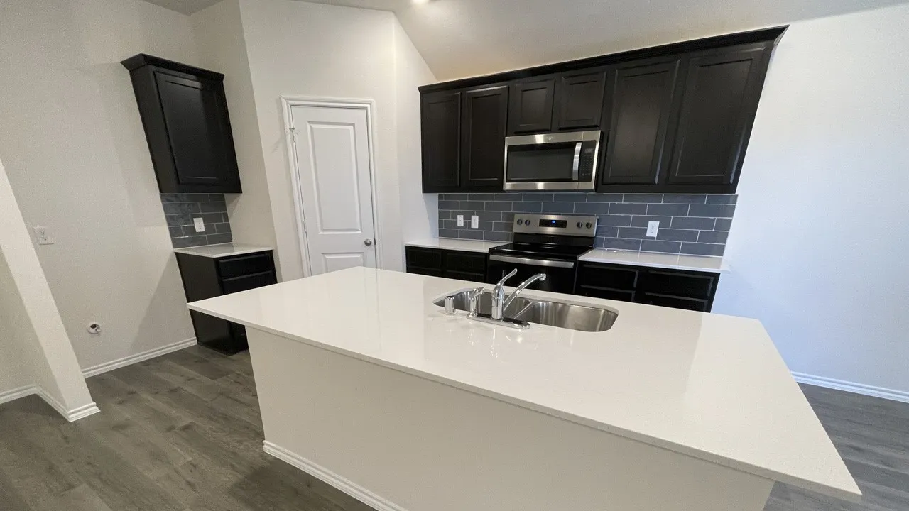 Kitchen featuring a large central island with an undermount sink, dark cabinetry, stainless steel appliances, subway tile backsplash, and wood-finish flooring