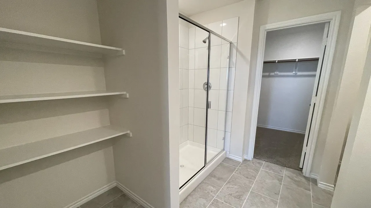 Built-in shelving, glass-enclosed shower, and a walk-in closet with carpet flooring