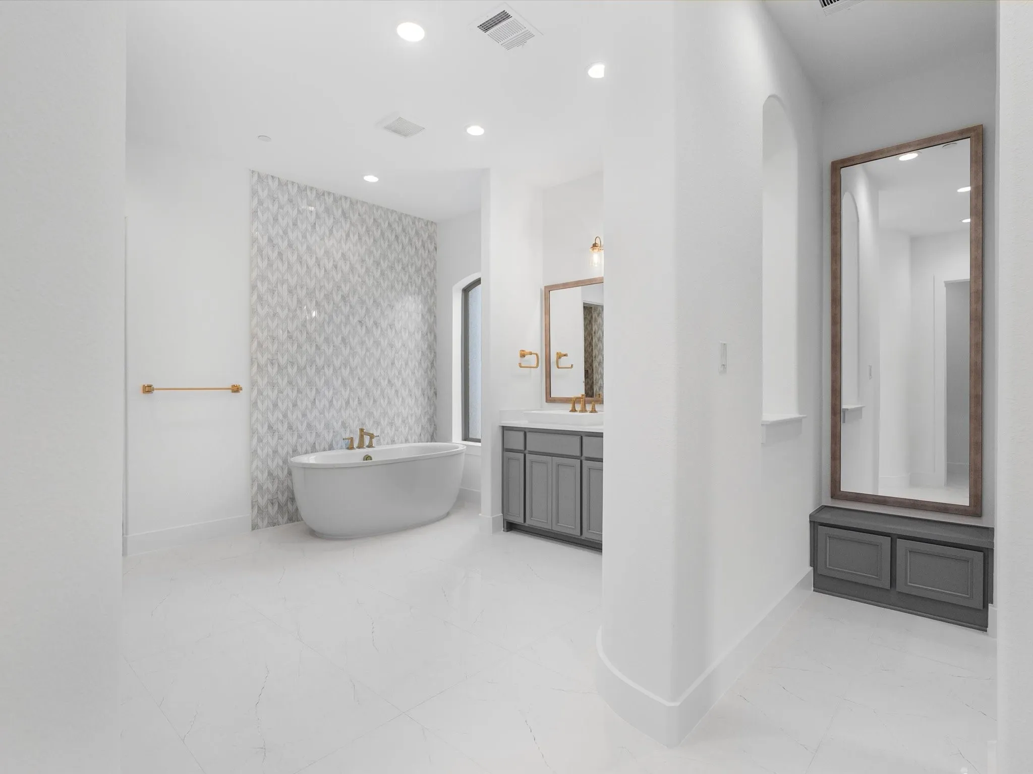Freestanding soaking tub, floor-to-ceiling accent tile, recessed lighting, double vanity with gray cabinetry, and arched architectural details