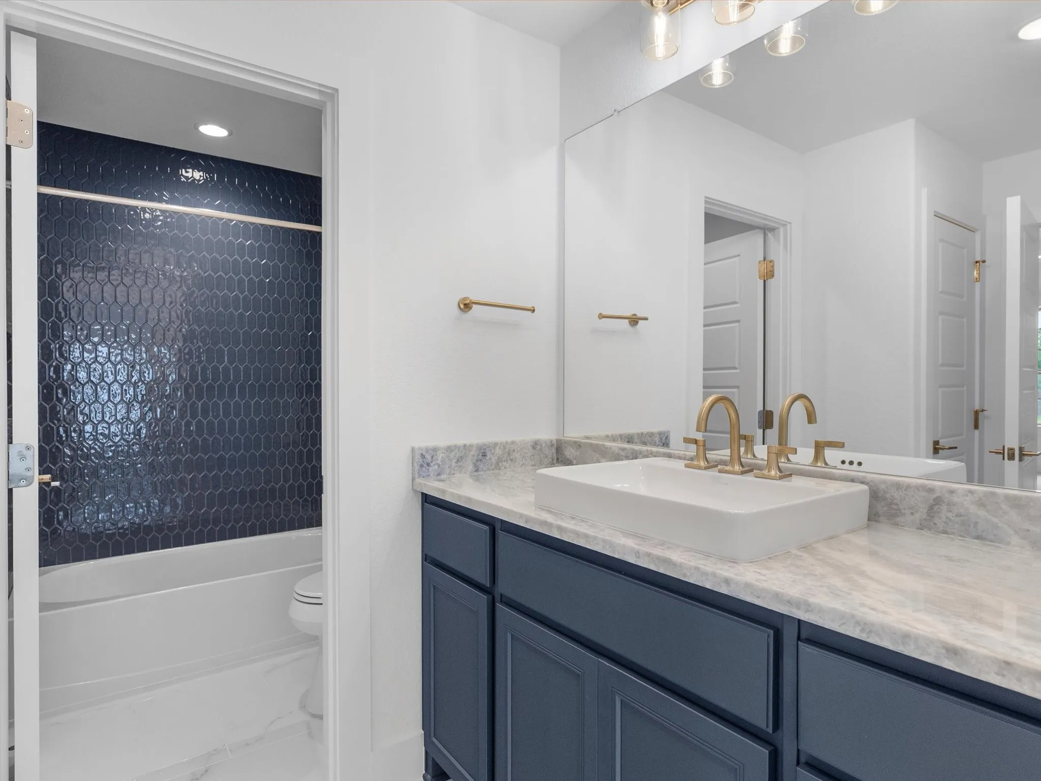 Vanity with dual gold-finish fixtures, vessel sink, blue cabinetry, and light-toned countertop