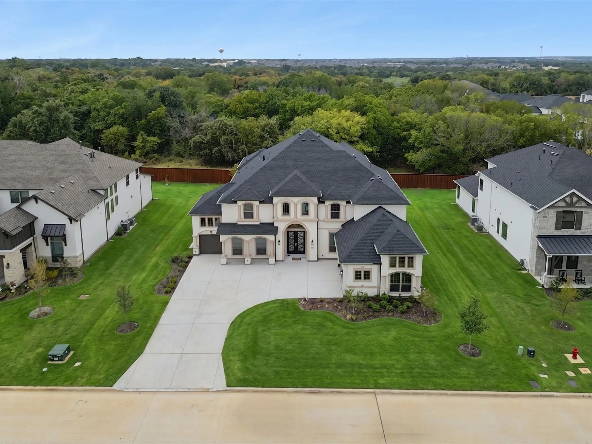 Stately stucco and stone exterior, dark shingle roof, attached garage, concrete driveway, and manicured lawn