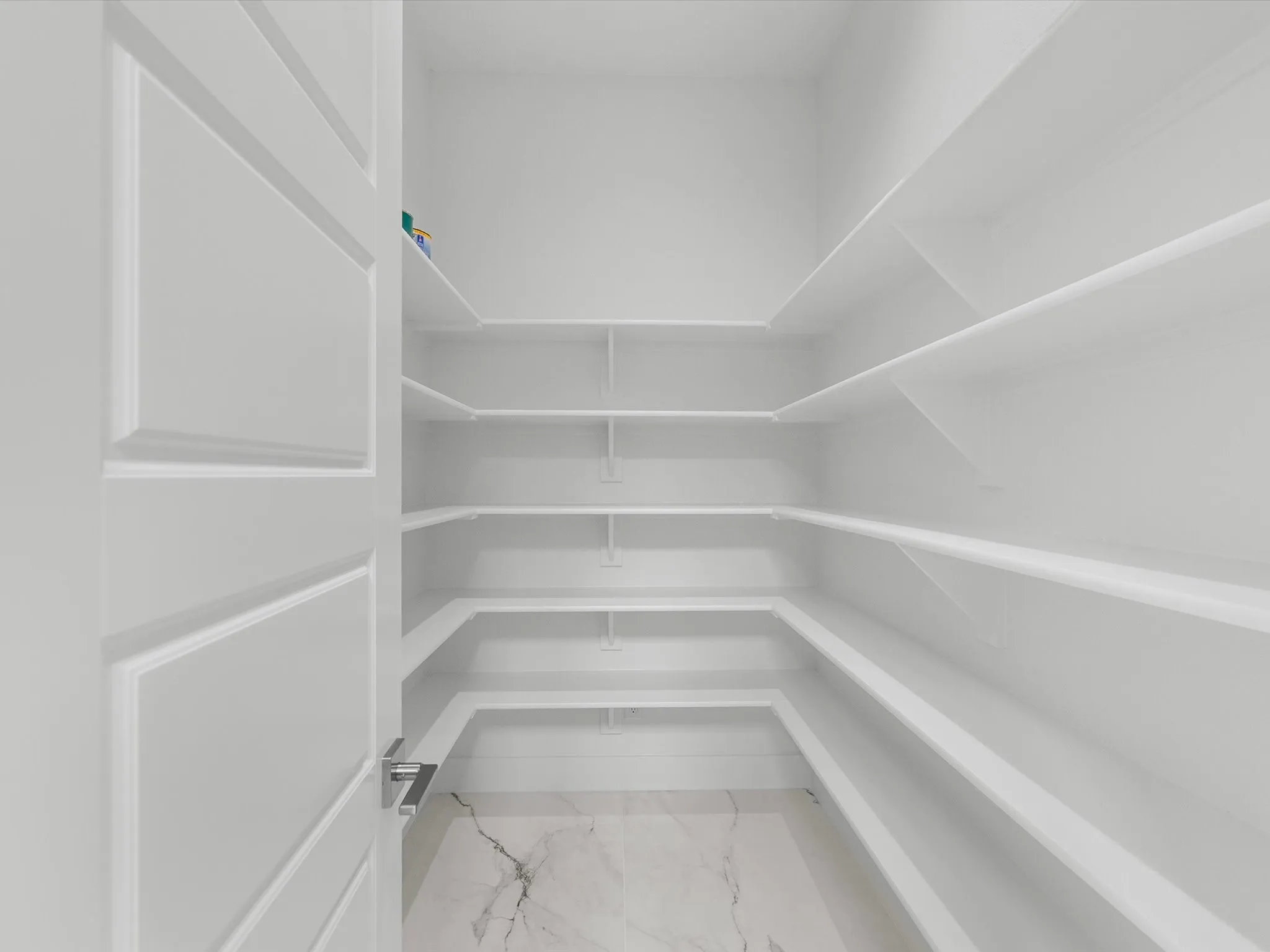 Walk-in pantry featuring extensive built-in shelving, white walls, and marble-look flooring