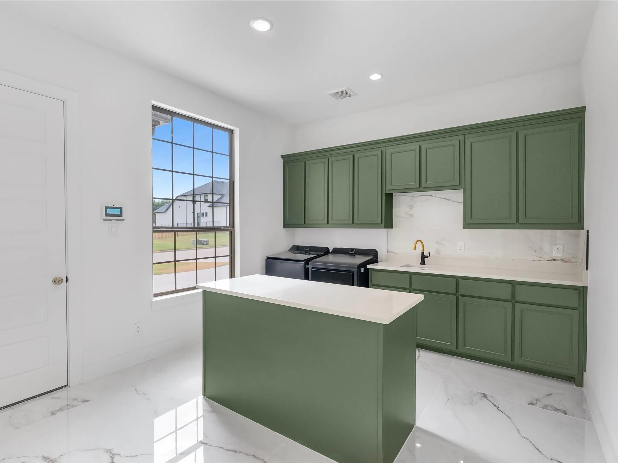 Green cabinetry, white countertop, white marble-look flooring, large multi-pane window, and recessed lighting