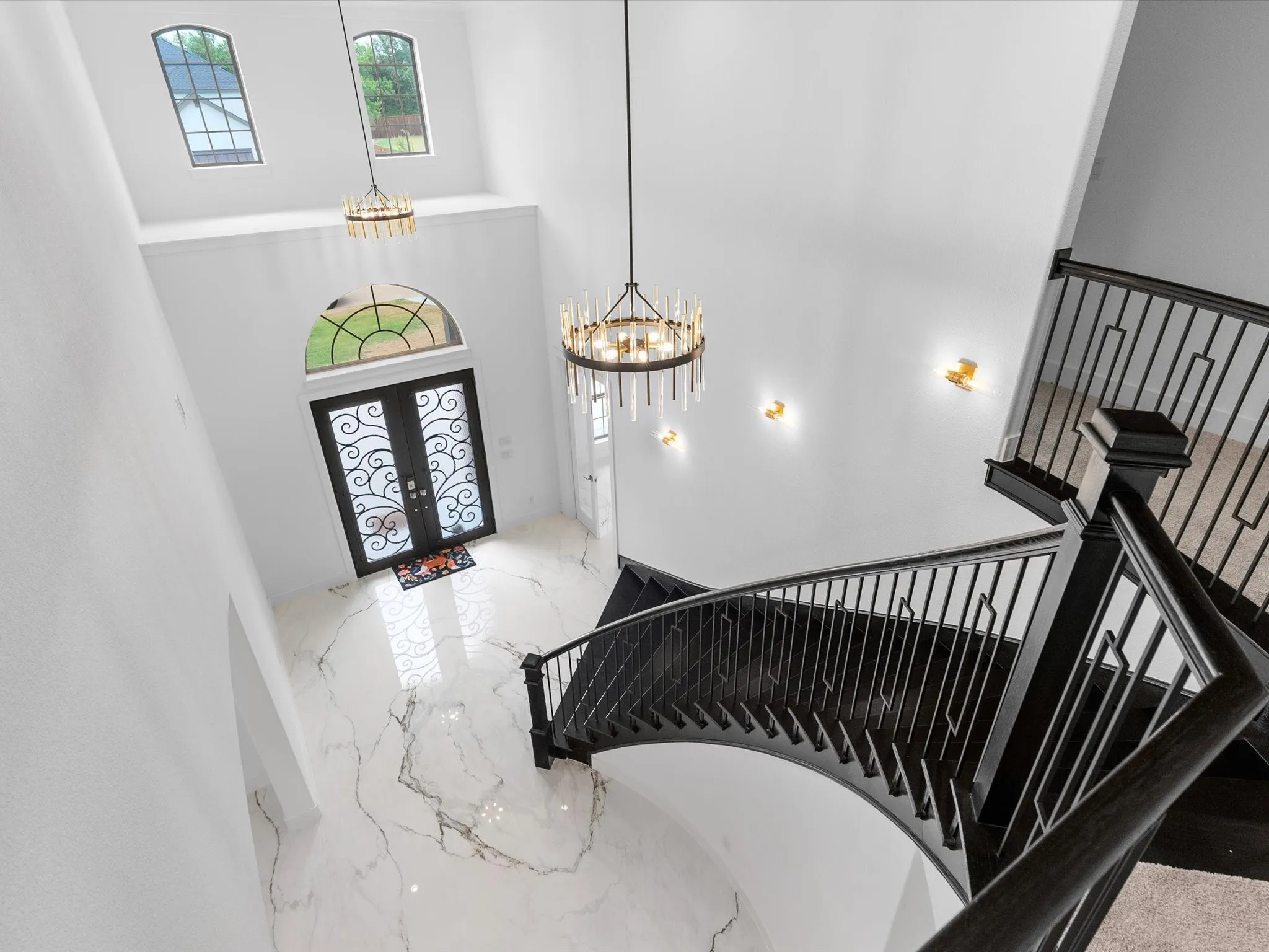 Two-story foyer with a curved staircase, marble-finish flooring, wrought iron double entry doors, and decorative chandeliers