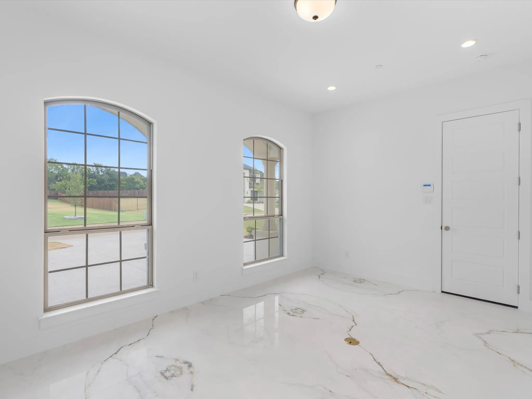 Arched windows, recessed lighting, ceiling-mounted light fixture, white interior door, and marble-look flooring