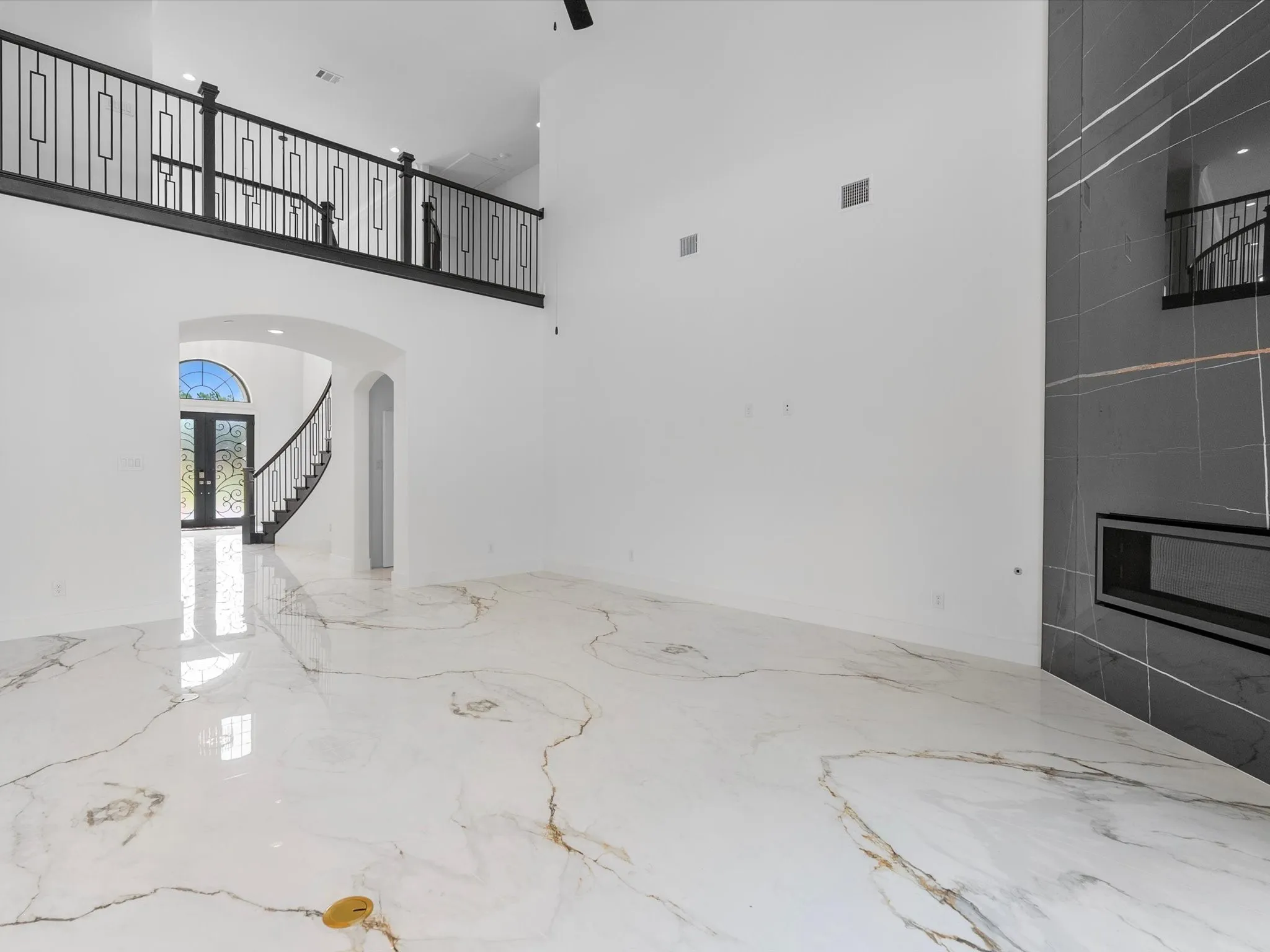 Two-story living area with high ceilings, large-format tile flooring, a sleek fireplace, and a second-story landing featuring decorative iron railings