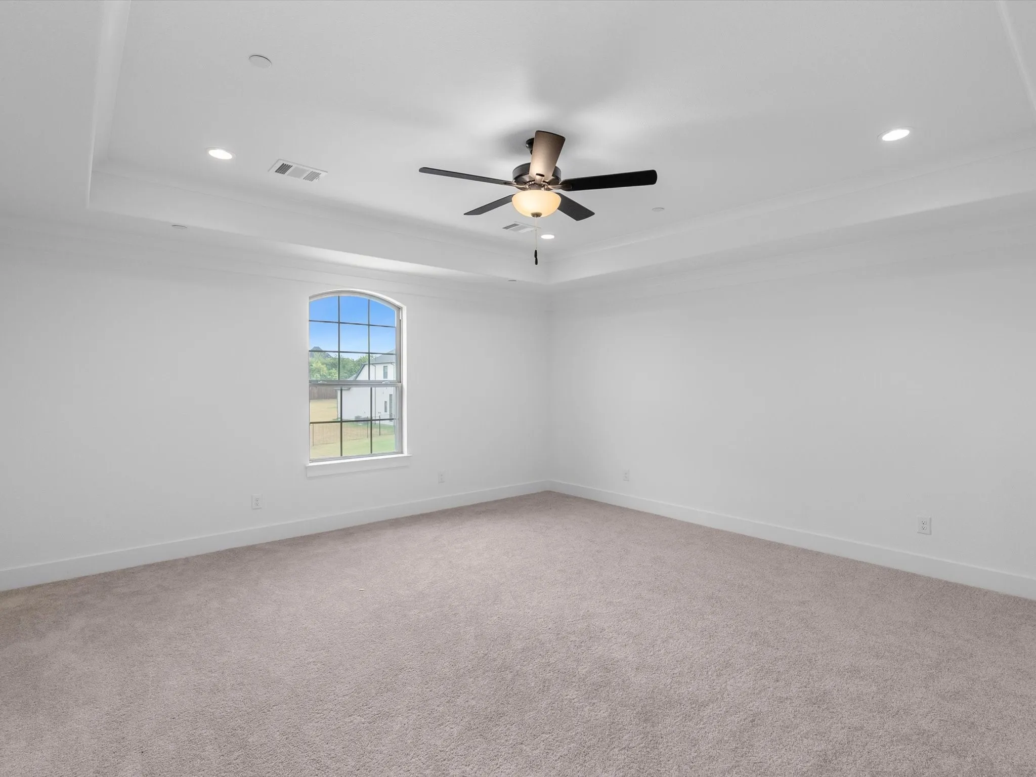 Tray ceiling with recessed lighting, ceiling fan, arched window, and neutral carpet flooring