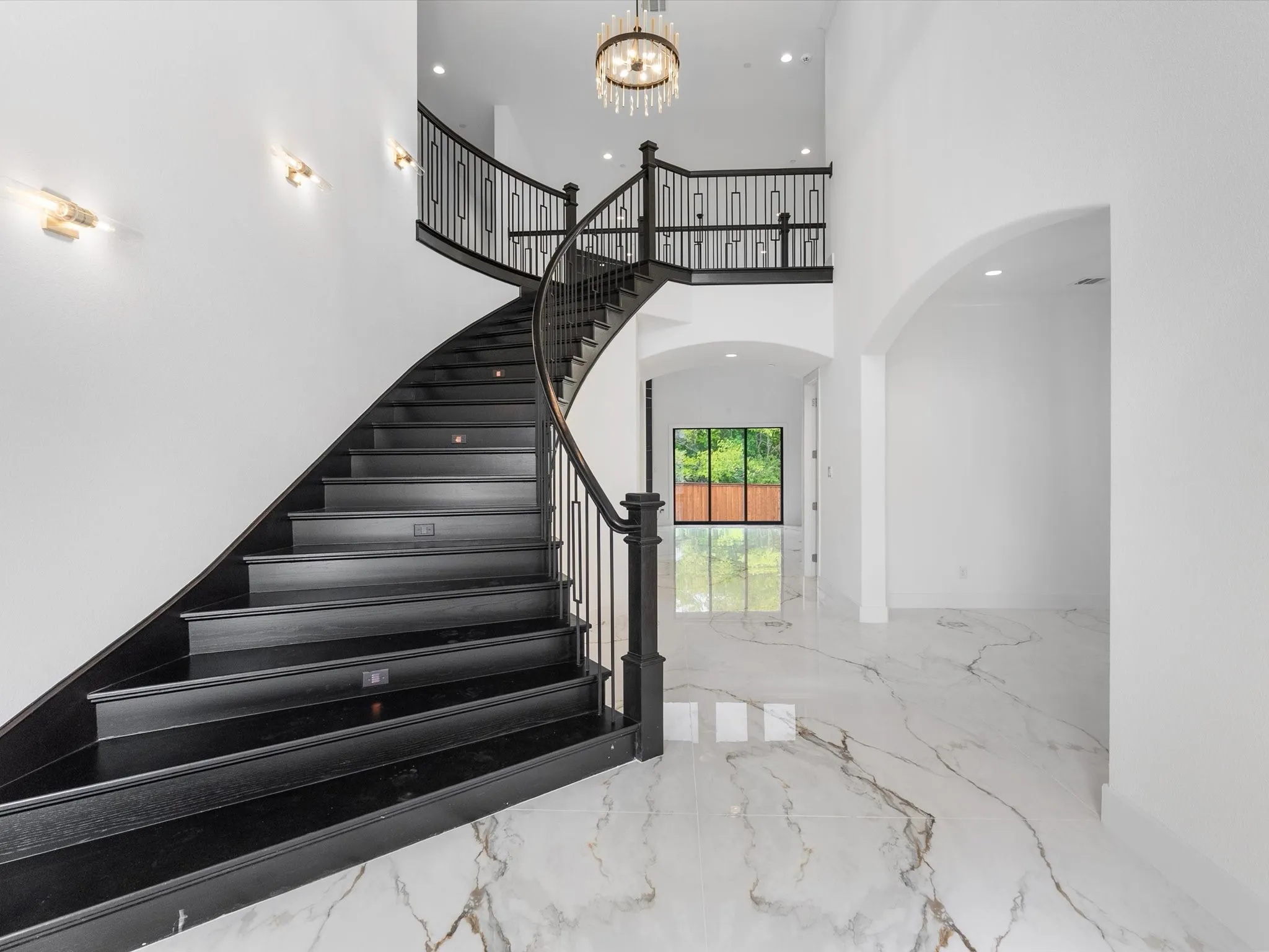 Grand entryway with a curved staircase, ornate iron balusters, high ceilings, and polished tile flooring