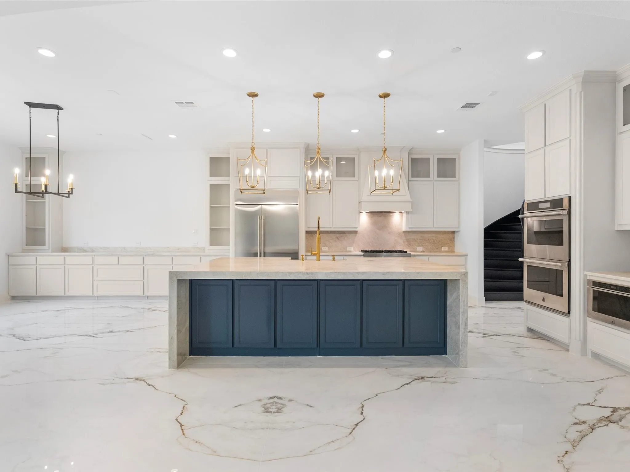 Spacious kitchen featuring a large island with blue cabinetry, white shaker-style perimeter cabinets, stainless steel appliances, and gold-tone pendant lighting