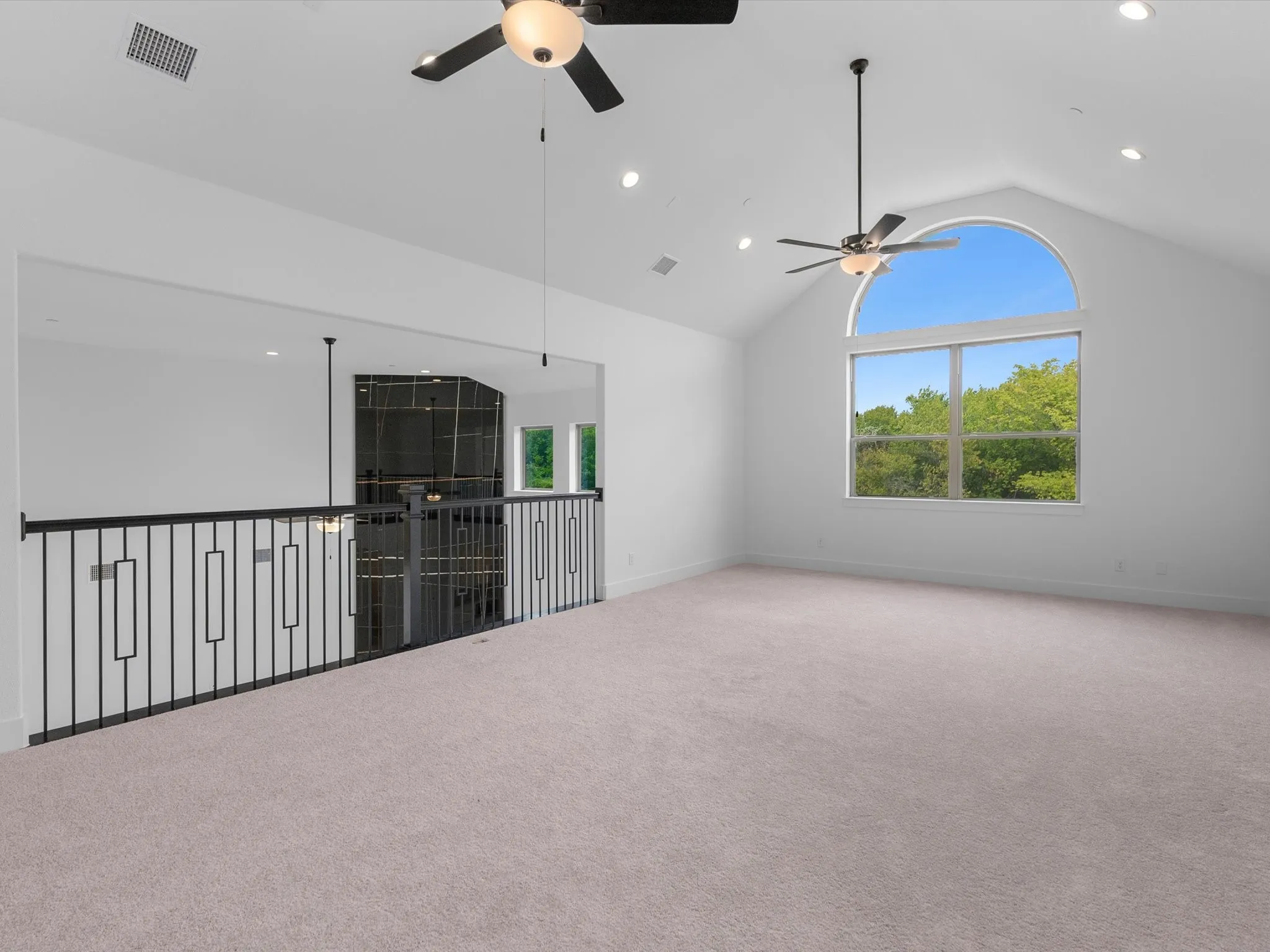 Arched window, vaulted ceiling, recessed lighting, two ceiling fans, and black metal railing